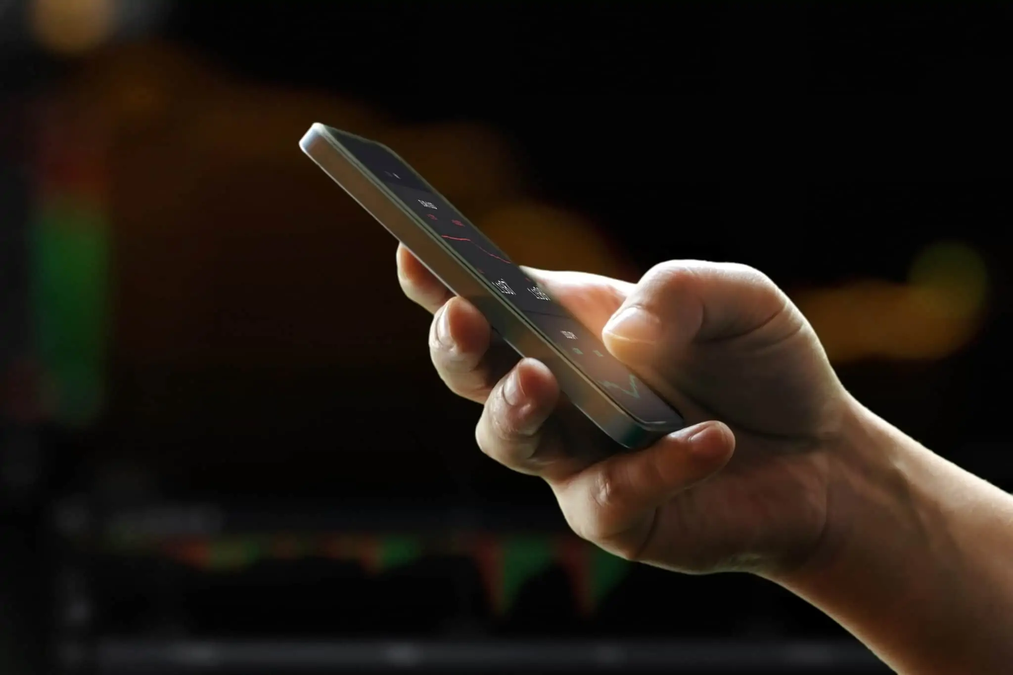 Mão de homem a segurar o telemóvel, através do qual analisa os seus investimentos realizados através de plataformas peer-to-peer