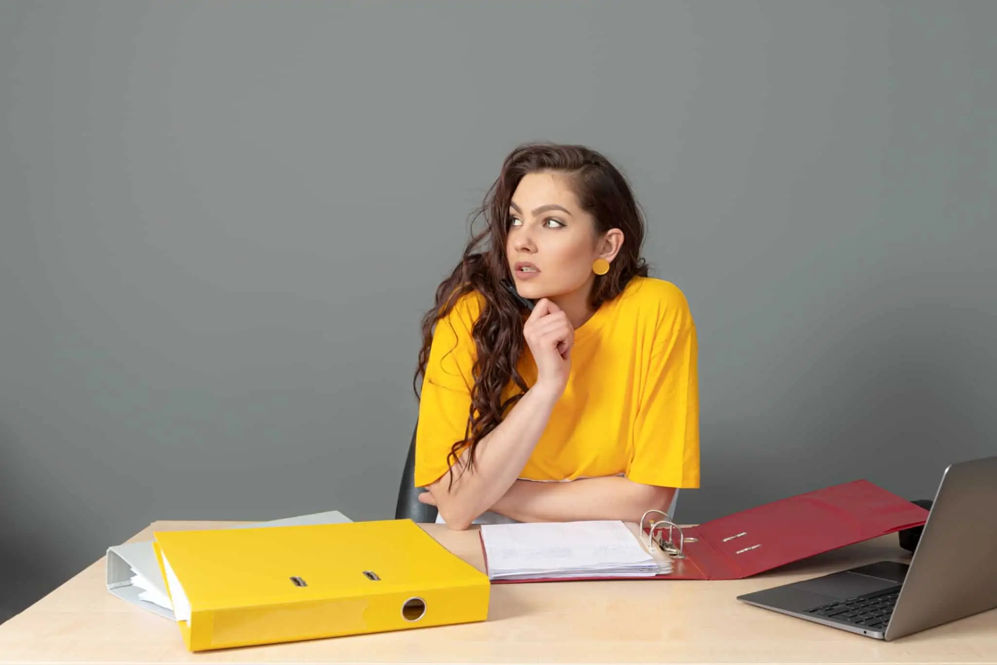 Trabalhar por conta de outrem ou ser empresário? 9 passos até à decisão jovem mulher, à mesa e em frente ao computador, está pensativa enquanto estuda dossiers sobre trabalhar por conta de outrem ou ser empresário