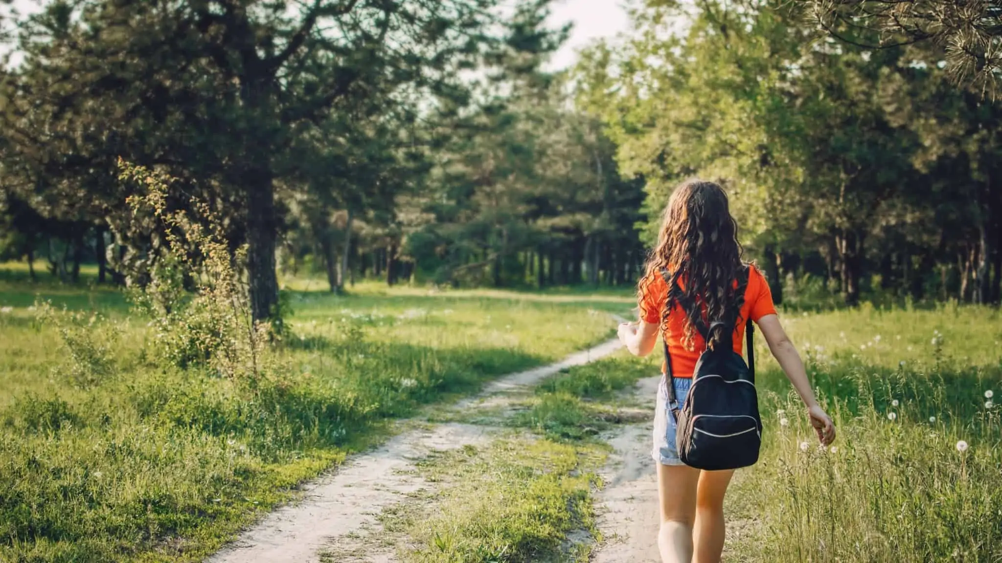 Feriados municipais facultativos: Como funciona? Jovem de mochila às costas, enquanto passeia numa floresta numa férias em famílias