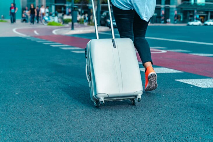 jovem estudante parte para o programa Erasmus. Dirige-se ao aeroporto, para uma entrada com mais jovens a aguardar, arrastando a sua mala de viagem.
