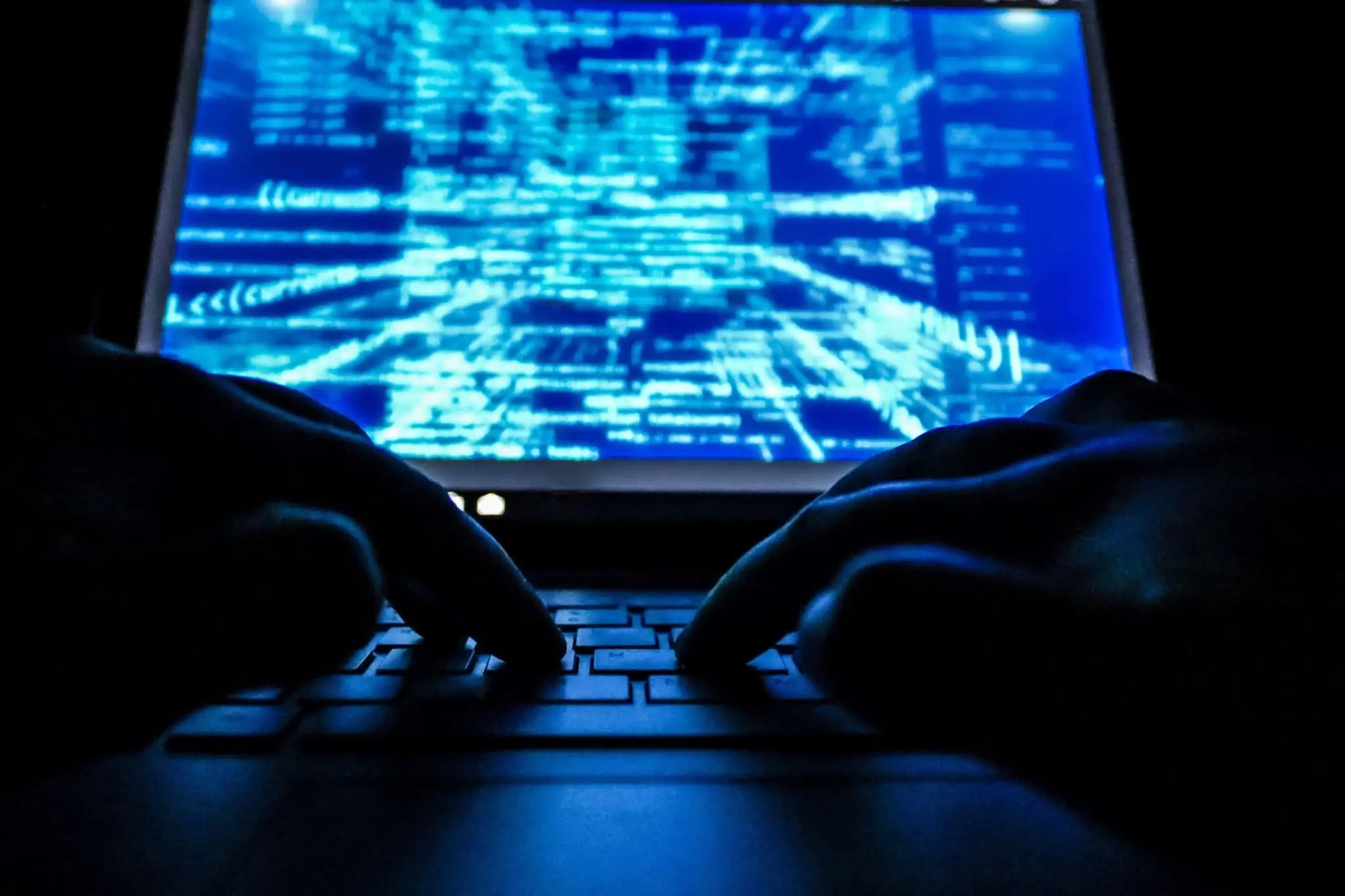 Cibercrimes: O que são? Saiba como prevenir e proteger-se foto ilustrativa do cibercrime com uma imagem escura, só com umas mãos num teclado do computador enquanto se visualizam estruturas informáticas no ecran