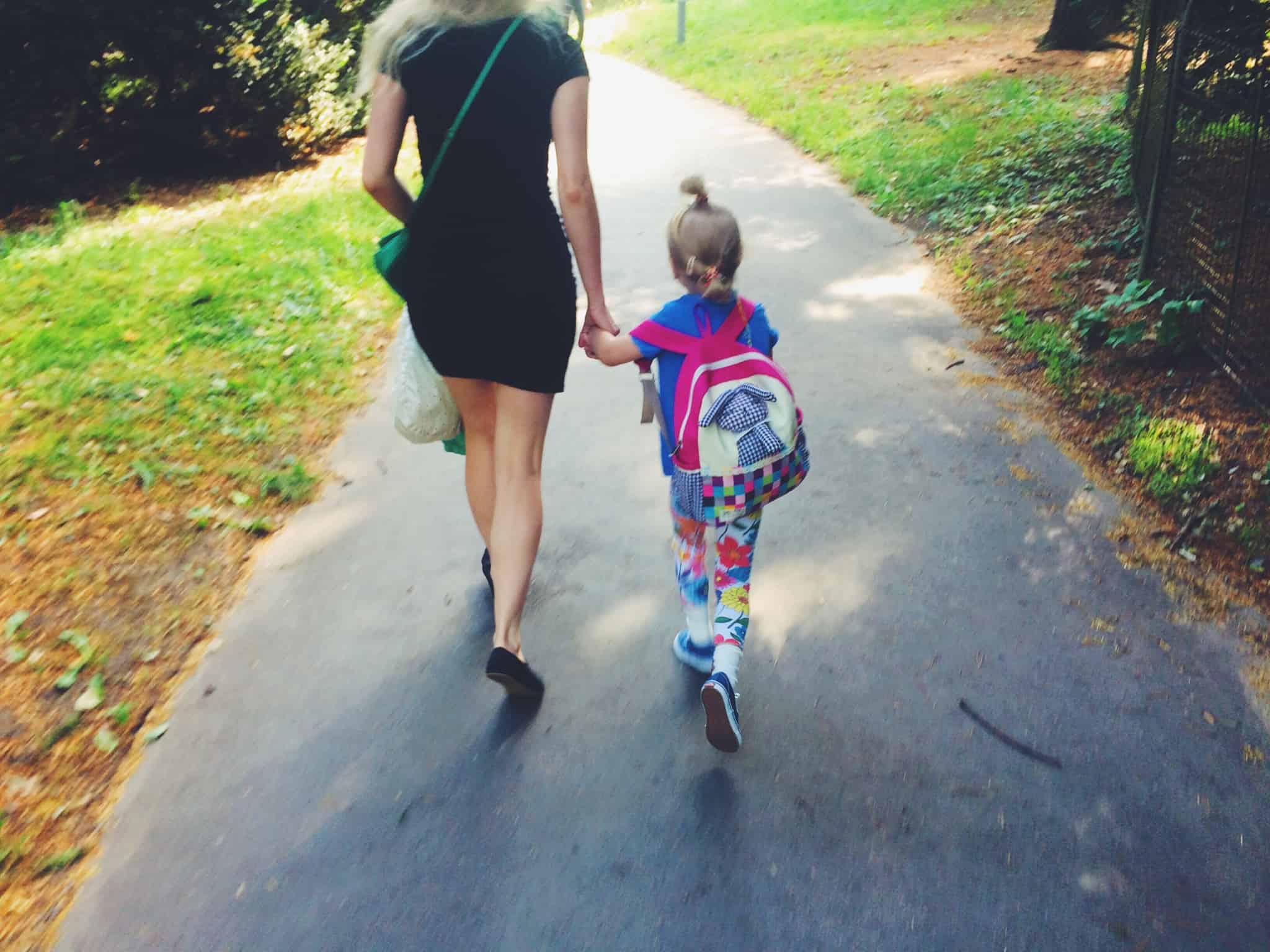 mãe caminha, de mãos dadas, com a filha pequena que vai para a escola pela primeira vez