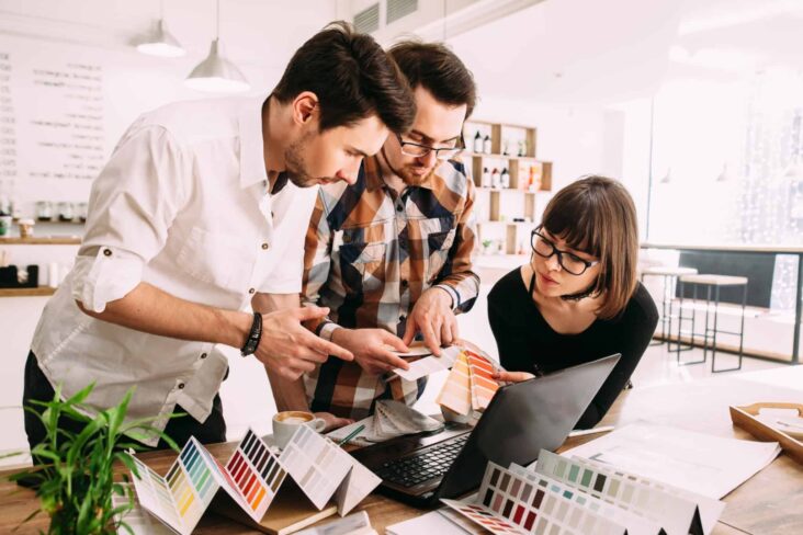 grupo de jovens (dois rapazes e uma rapariga), em ambiente de escritório, trabalham em equipa na escolha de materiais.