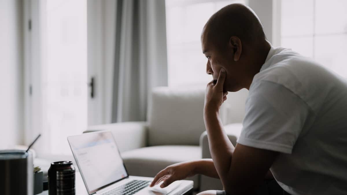 Senhor pensativo sentado num sofá à frente de um portátil