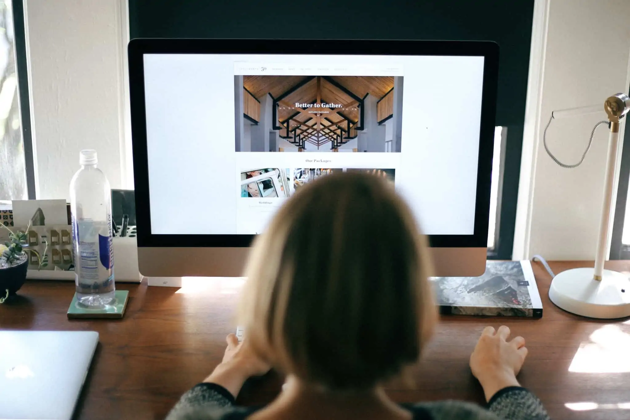 Precisa de criar um site para o seu negócio? Siga estes seis passos jovem mulher está ao computador, apoiada por um grande ecran, a criar e desenvolver um site para promover um negócio, uma marca.