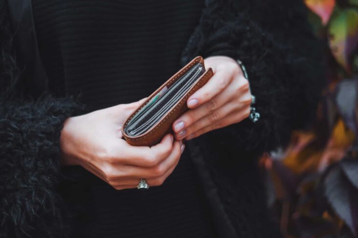produção fotográfica em que se vê apenas o plano das mãos de uma mulher que seguram uma carteira, com documentos de identificação