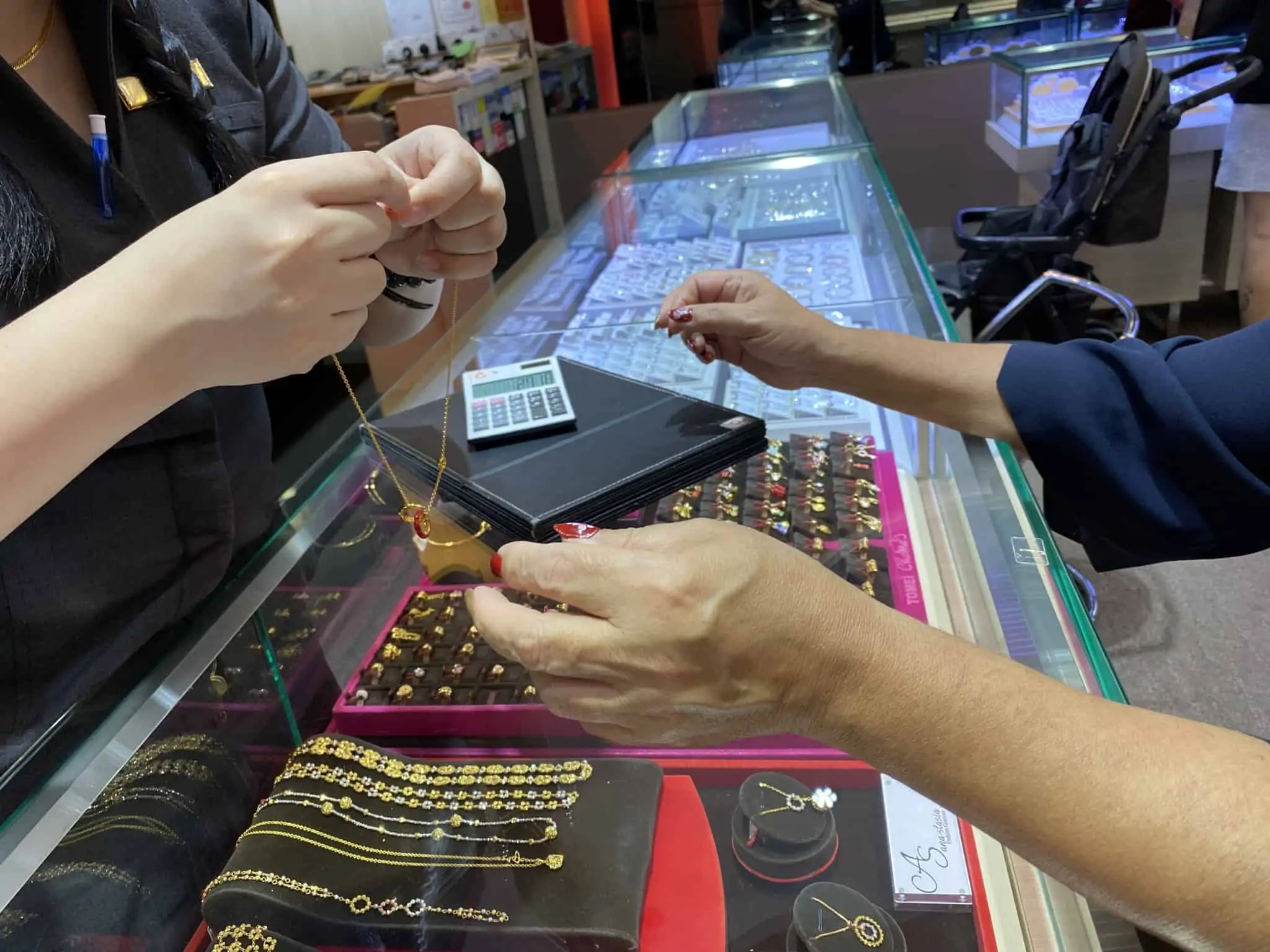 jovem mulher atende, numa loja de venda de ouro, uma jovem cliente que está a escolher qual a peça a comprar