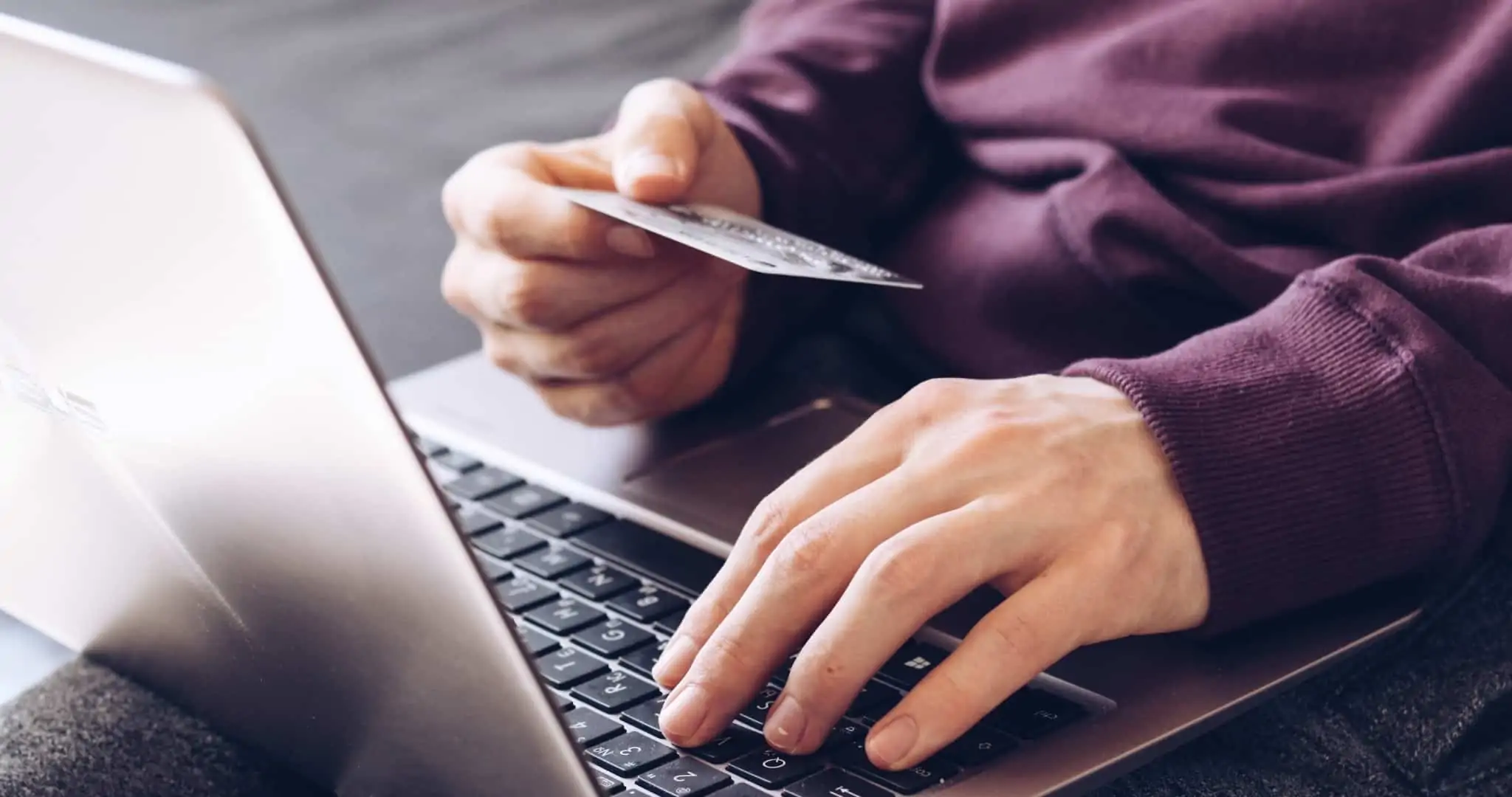 Apostas online: quando posso levantar o meu dinheiro? Rapaz com portátil ao colo e cartão na mão a levantar dinheiro online de apostas