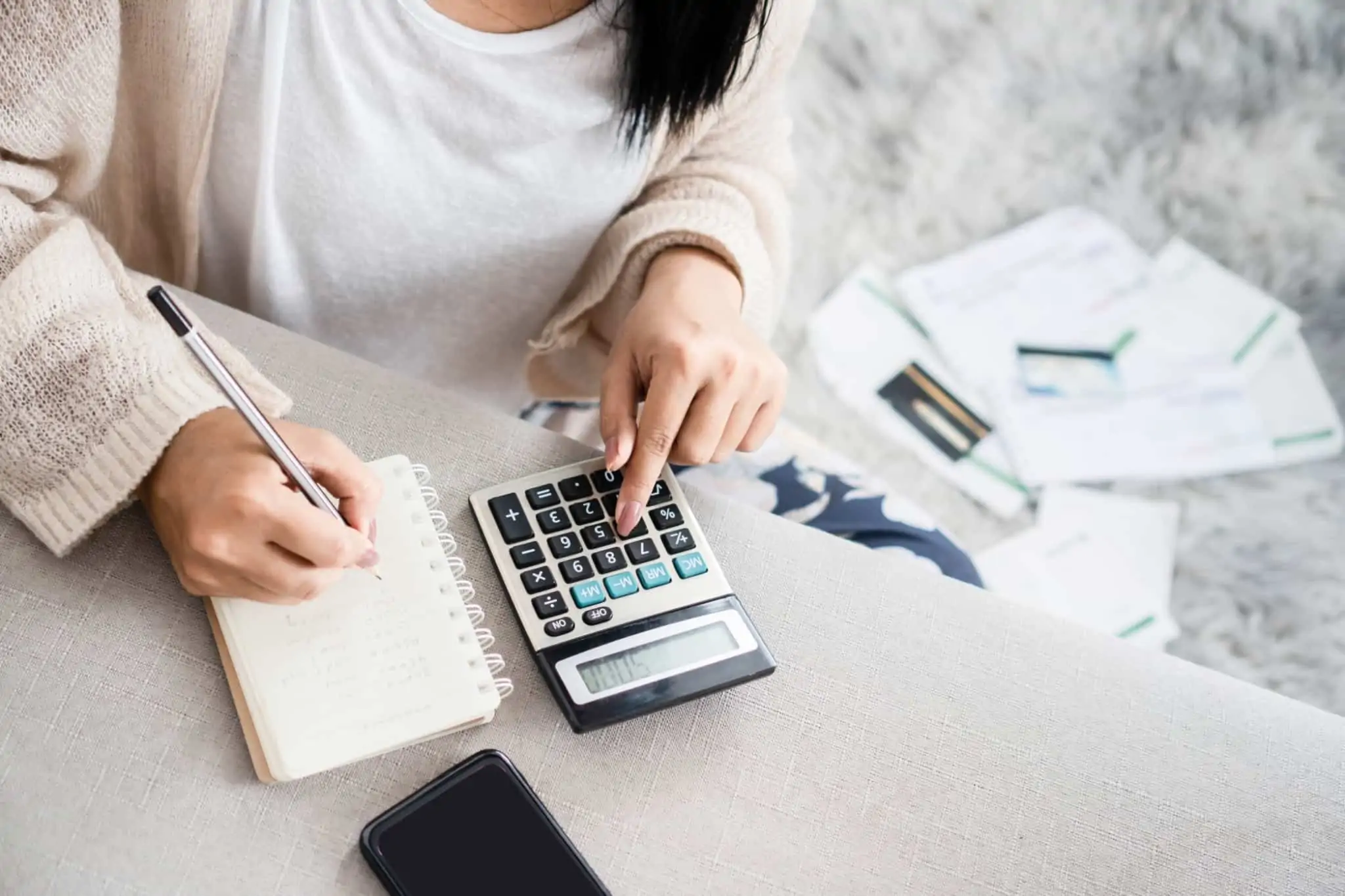 Leasing: o que é e como funciona? Imagem de uma mulher a fazer contas numa calculadora e com um bloco de notas - papéis, crédito, incumprimento