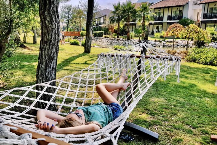 jovem mulher deitada numa cama de rede, no relvado frente à sua casa de férias