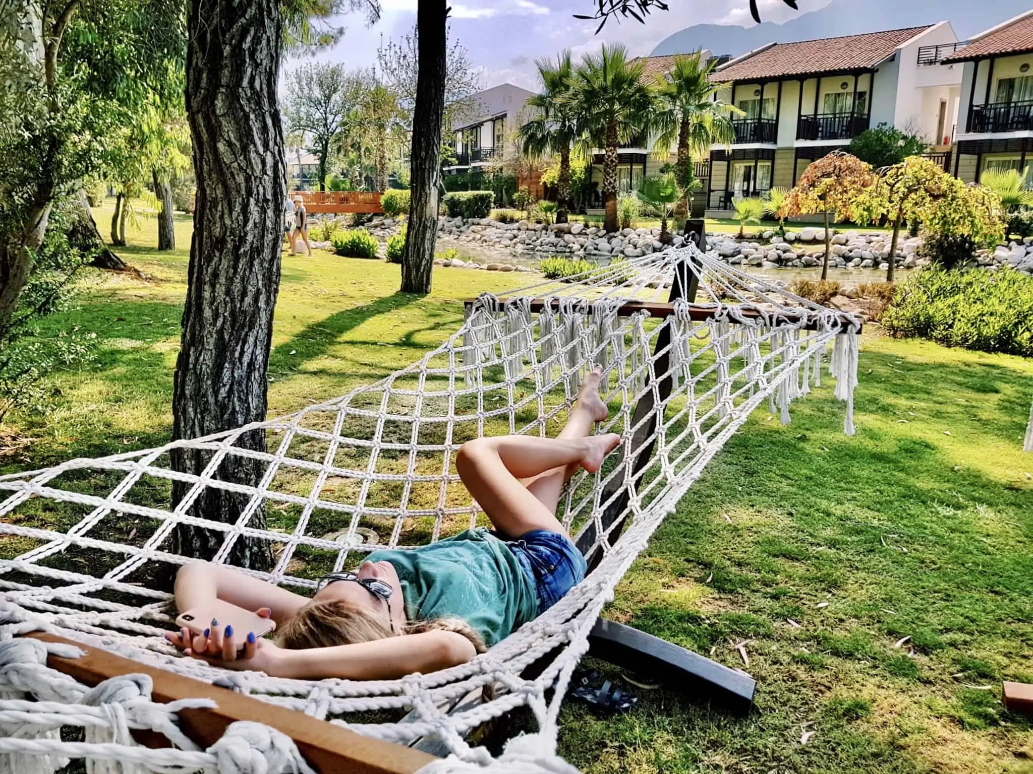 Vai comprar uma casa de férias? O que deve ter em conta antes de decidir jovem mulher deitada numa cama de rede, no relvado frente à sua casa de férias