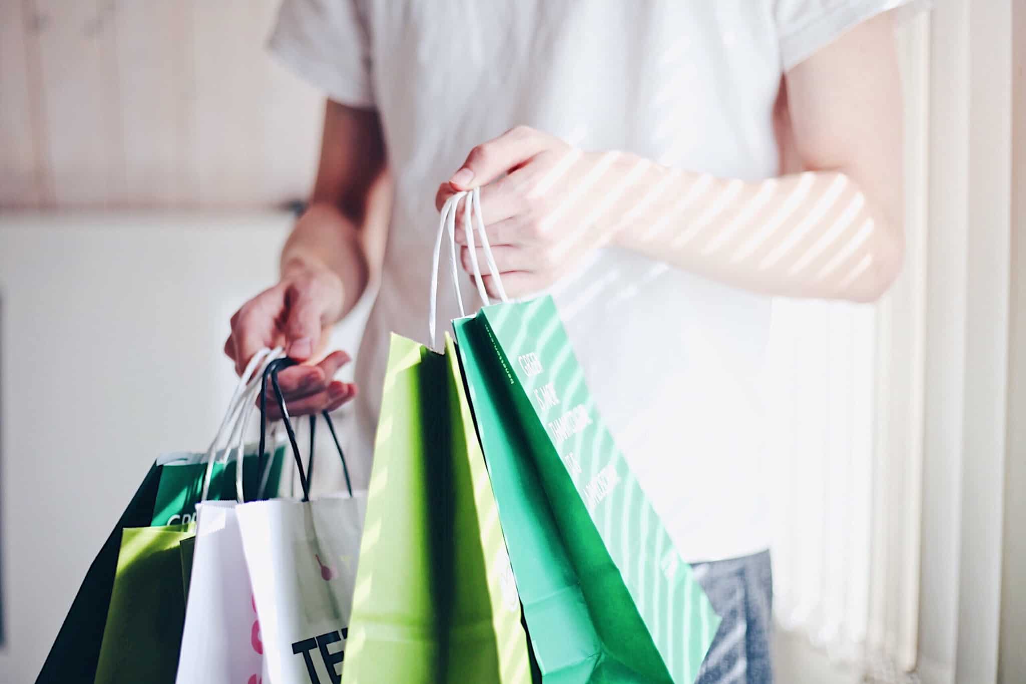 Não planeia as suas compras? Estas 6 dicas de poupança são para si compras e dicas de poupança ilustradas por uma produção fotográfica que mostra a mão de uma jovem que segura muitos sacos de compras