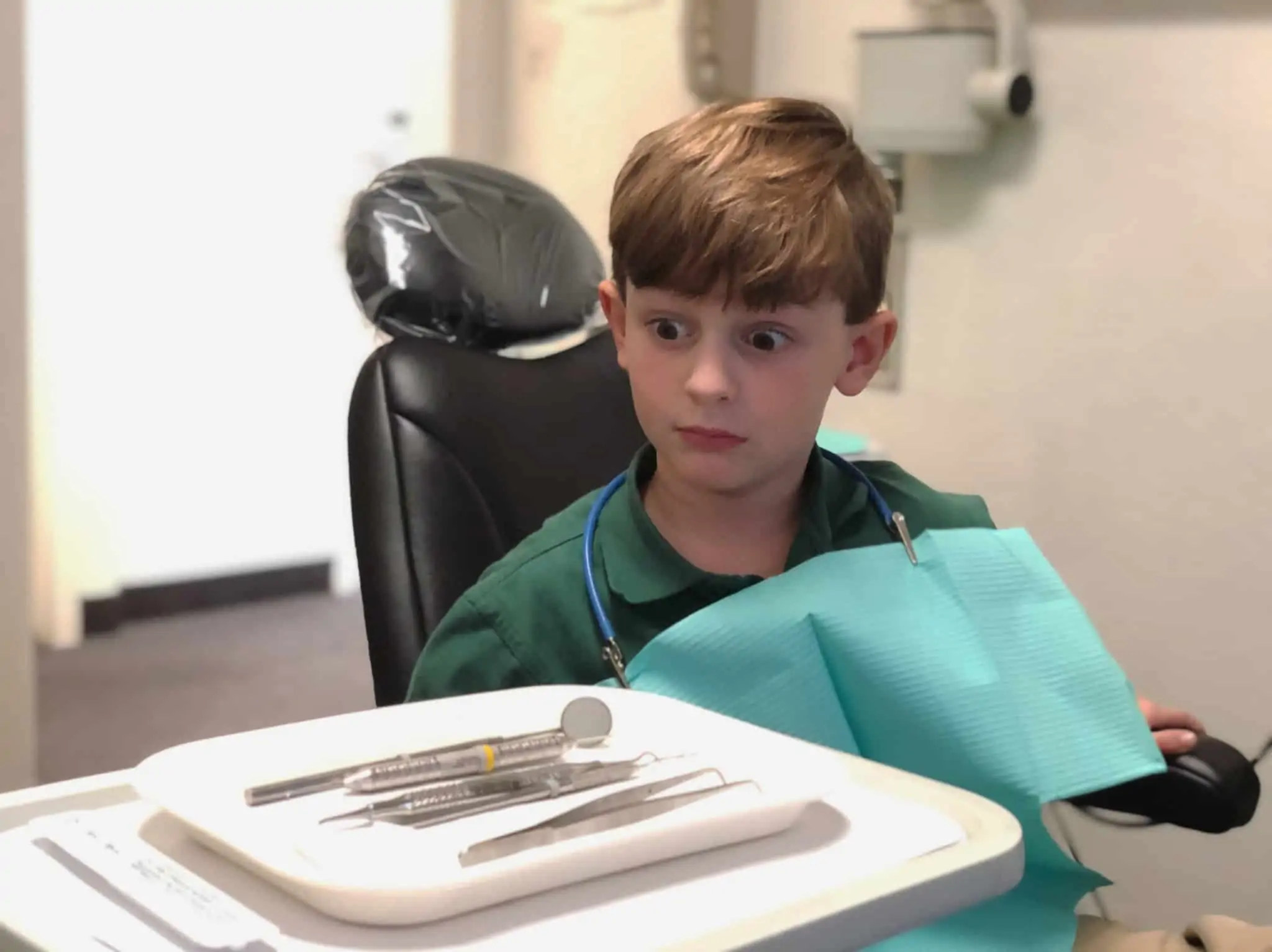 O seguro dentário cobre implantes? E aparelho? menino em consulta no dentista, já preparado, olha estupefacto e cheio de medo para os utensílios que vão ser usados pelo médico