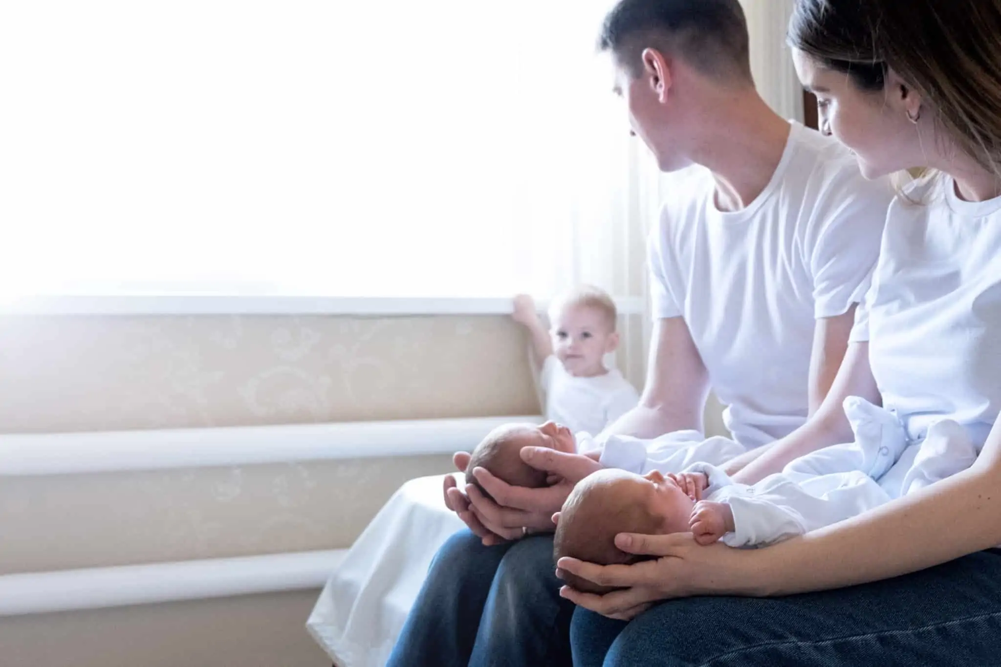 Apoios para famílias numerosas: Quais são e como pode obtê-los? jovem casal segura nos respetivos colos os seus recém nascidos, acompnhados pelo terceiro, e pequenbo, filho