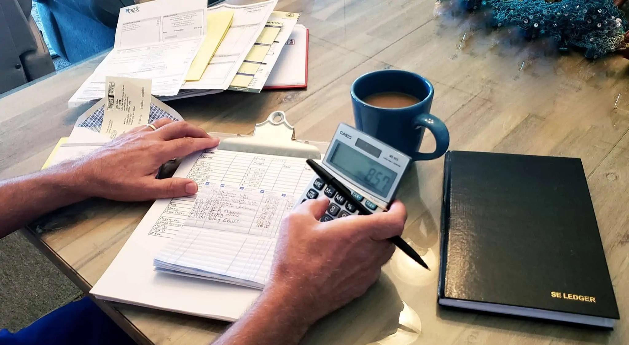 Juros de mora: Saiba em que situações se aplicam e quanto vai pagar jovem homem faz calculos, recorrendo a uma calculadora, analisando um série de contas espalahdas em cima da sua mesa