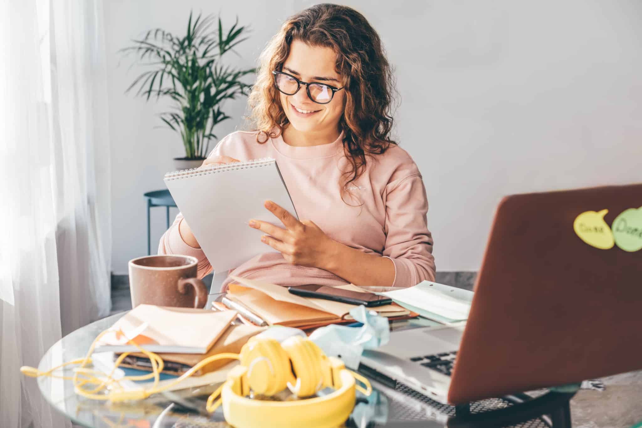jovem mulher, muito sorridente, sentada à mesa na sala da sua primeira casa, estuda o seu orçamento mensal