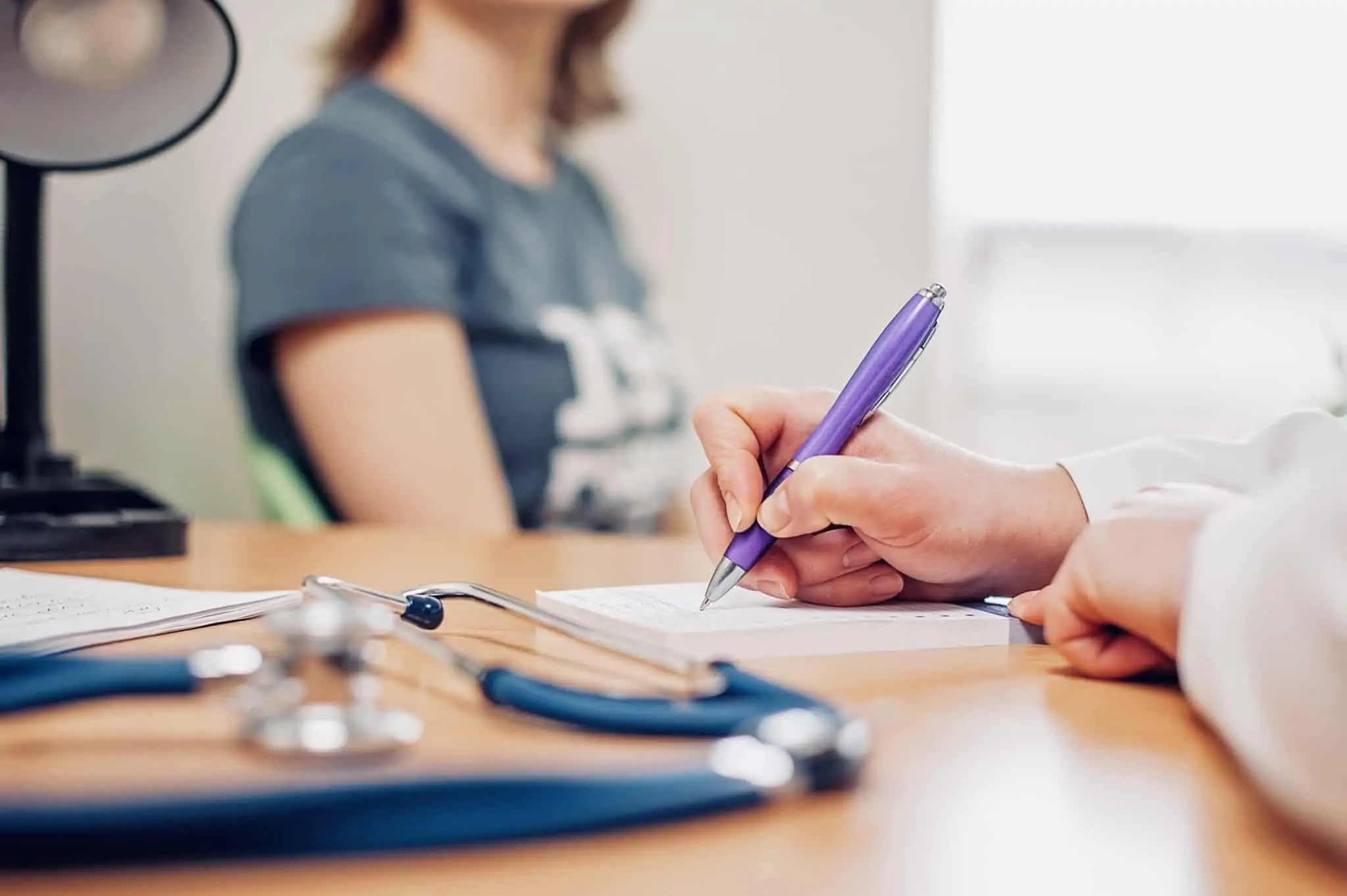 Seguro ou cartão de saúde? O que ter em conta antes de decidir jovem mulher em consulta médica aguarda a prescrição que o médico está a redigir