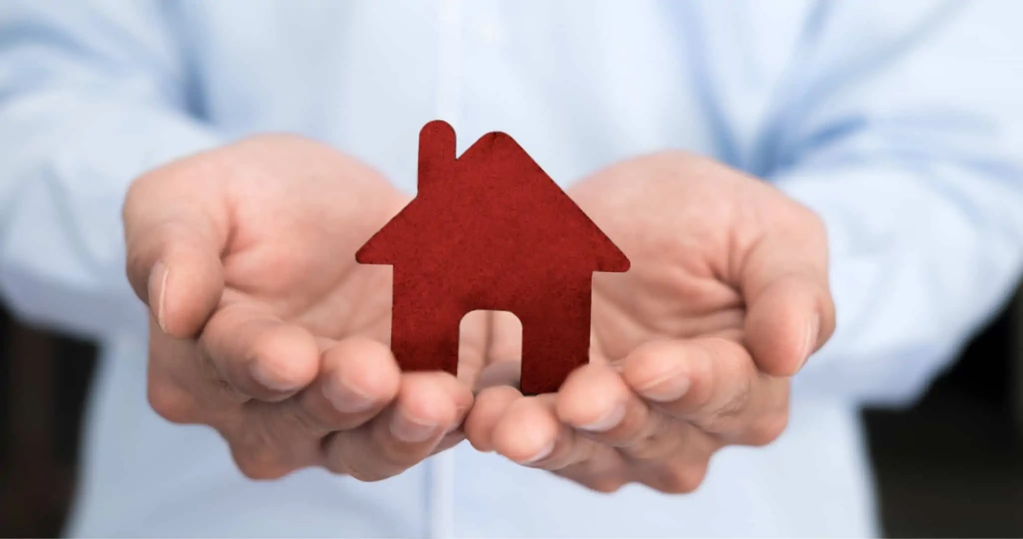 Como funciona o seguro de vida num crédito habitação? Mãos de homem a segurar peça em madeira de casa a simbolizar crédito habitação