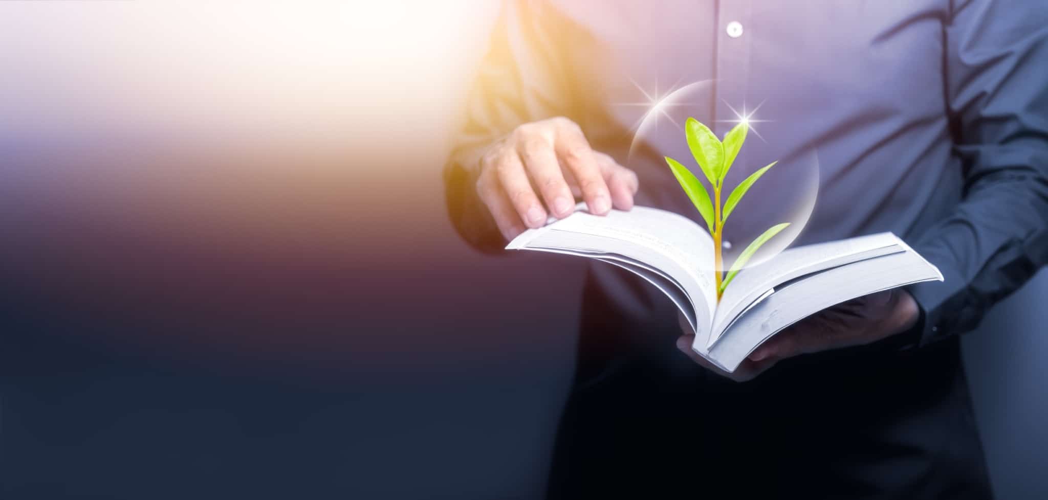 homem segura um livro aberto de onde sai uma pequena planta a despontar