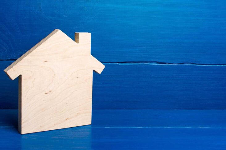 investimento imobiliário ilustrado com produção fotográfica que mostra uma casa em madeira , em fundo azul, liso