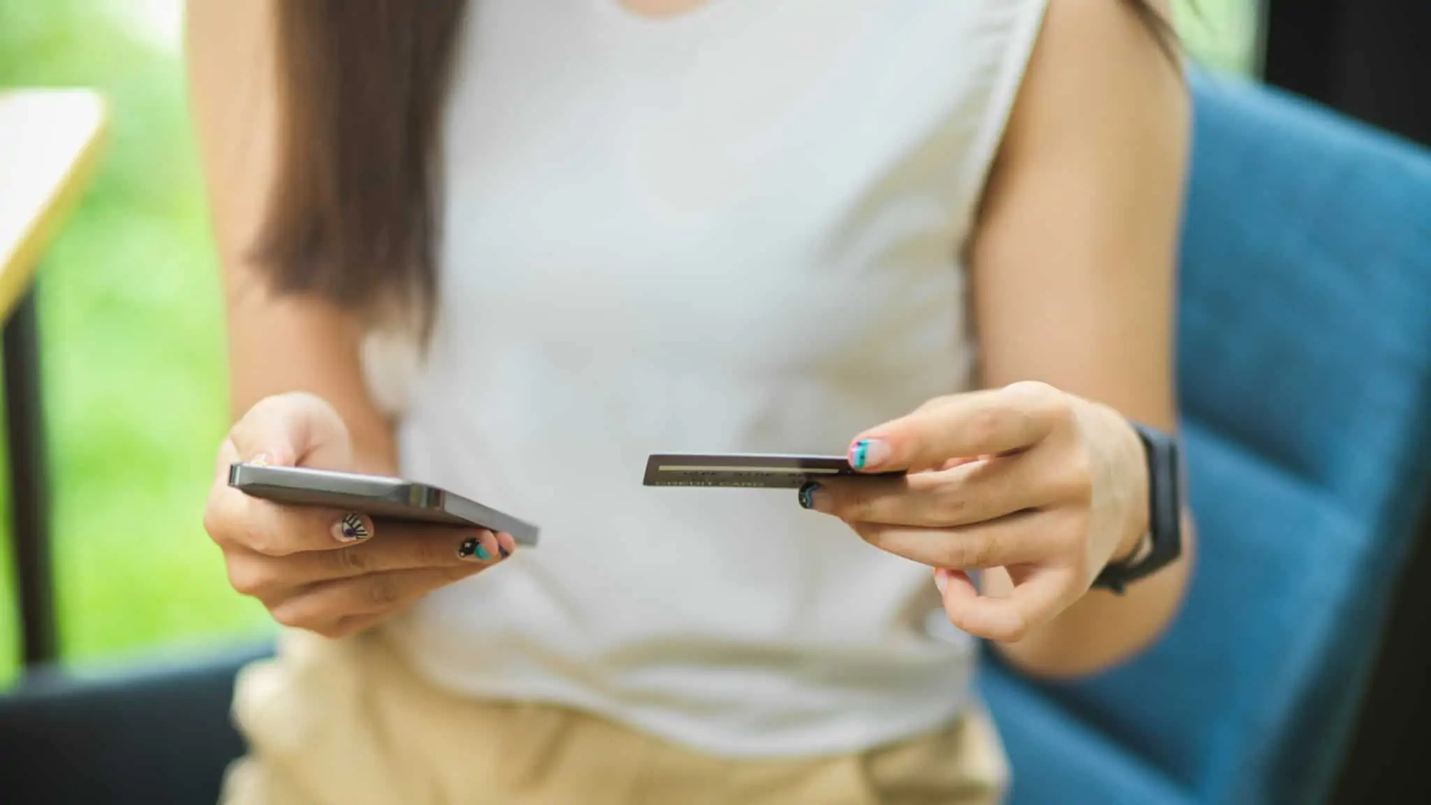 7 dicas para reduzir a sua pegada ambiental nas operações financeiras jovem mulher segira cartão de crédito e telemóvel que está a usar para fazer um pagamento