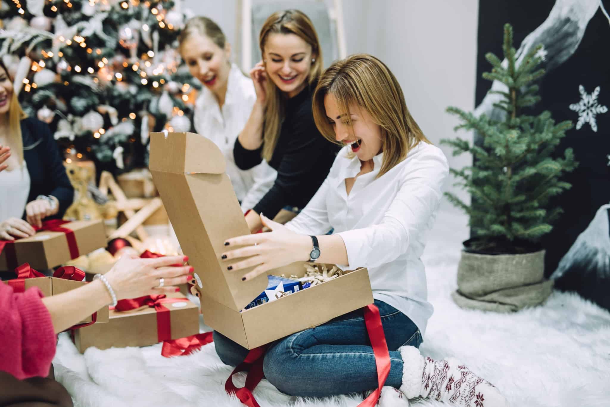 grupo de amigas, em abiente de felicidade e alegria, abrem os presentes junto à arvore de Natal