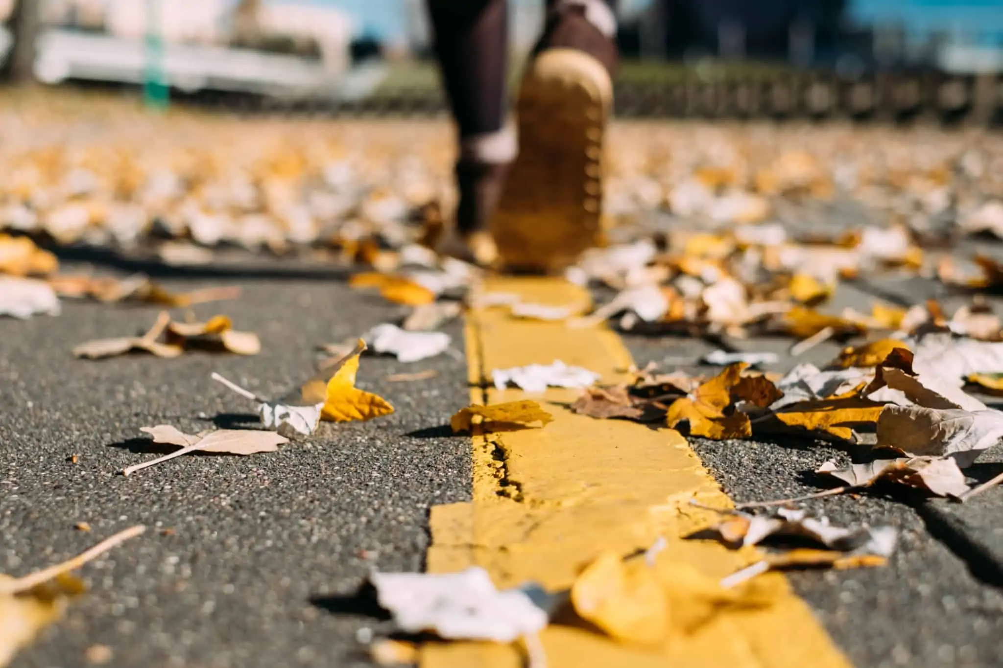 Seguro acidentes de trabalho: Quando acionar e qual o valor a receber? pés de um jovem a caminhar pela estadra repleta de folhas das árvores, amarelas, típicas do outono e inverno