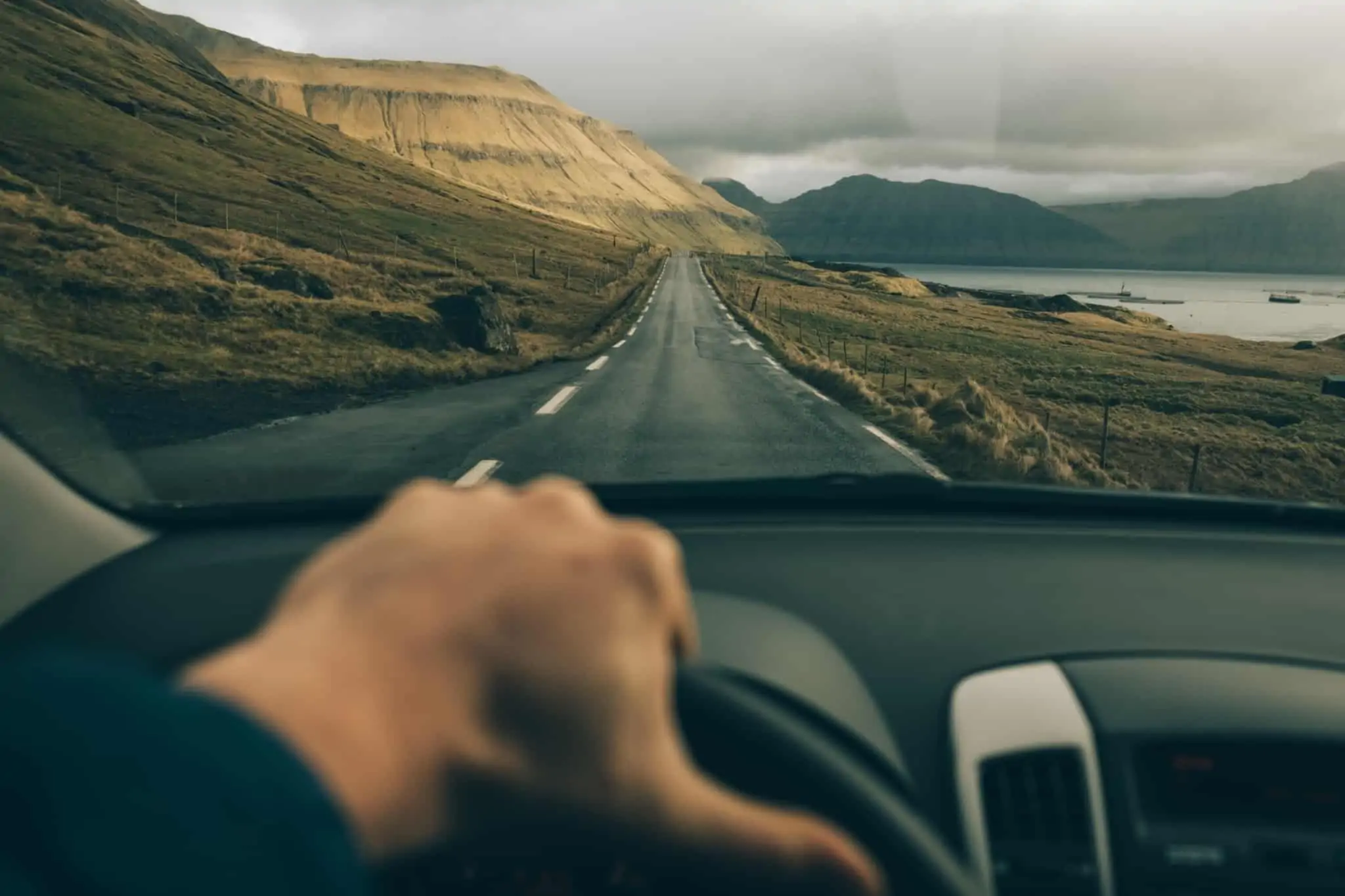 mão no volante de um automóvel que percorre uma estrada longa no meio da natureza