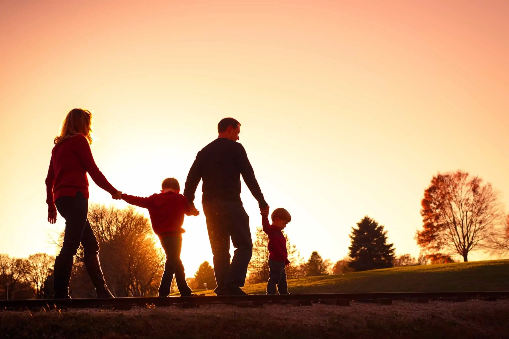 Seguro de vida: Como acionar em caso de morte pai e mãe caminham de mãos dadas, entre a natureza, com os dois filhos pequenos com o pôr de sol no horizonte