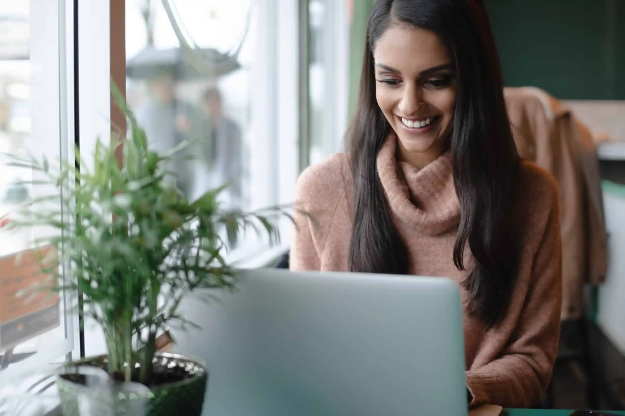 Como obter um rendimento extra através dos seus hobbies? Mulher sentada ao computador, de sorriso rasgado, enquanto trabalha