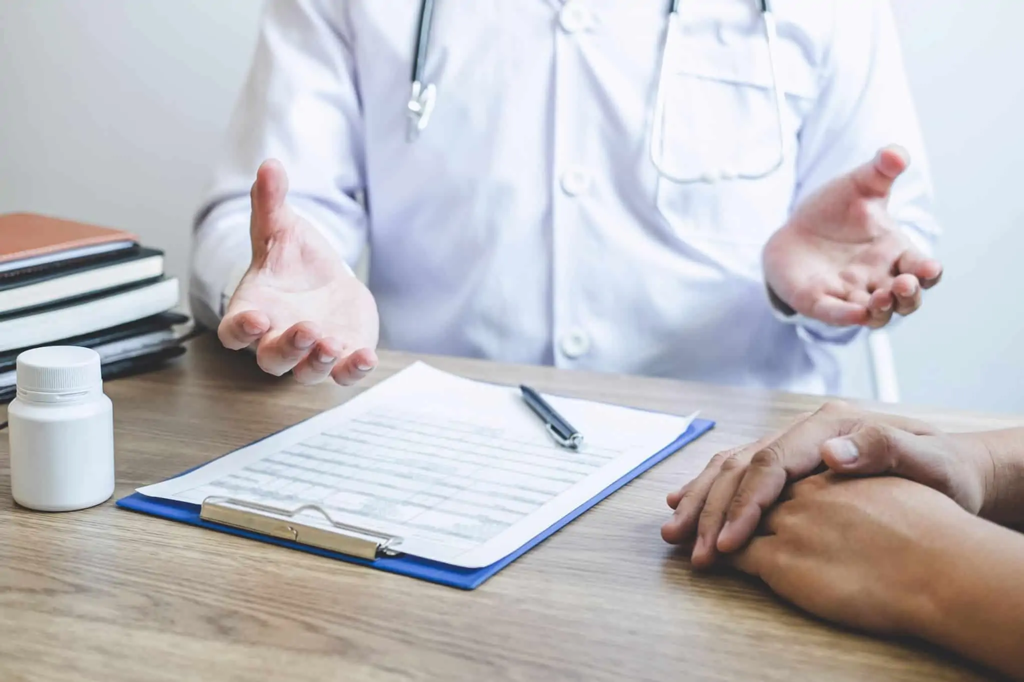 Imagem de um médico a explicar algo a um paciente - papeis e caneta em cima da mesa - pensões