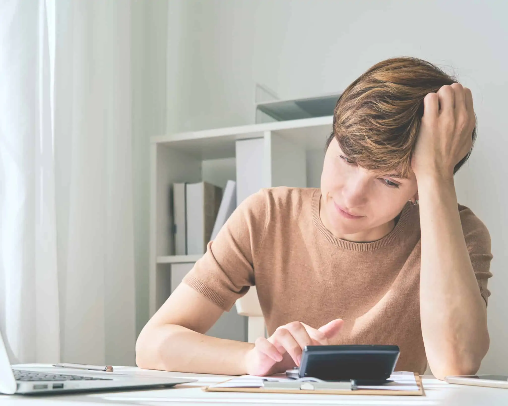 Tem dívidas em cartões de crédito? 7 dicas para recuperar a estabilidade jovem mulher com a mão na cabeça e olhar preocupado faz contas, às suas dívidas, na calculadora