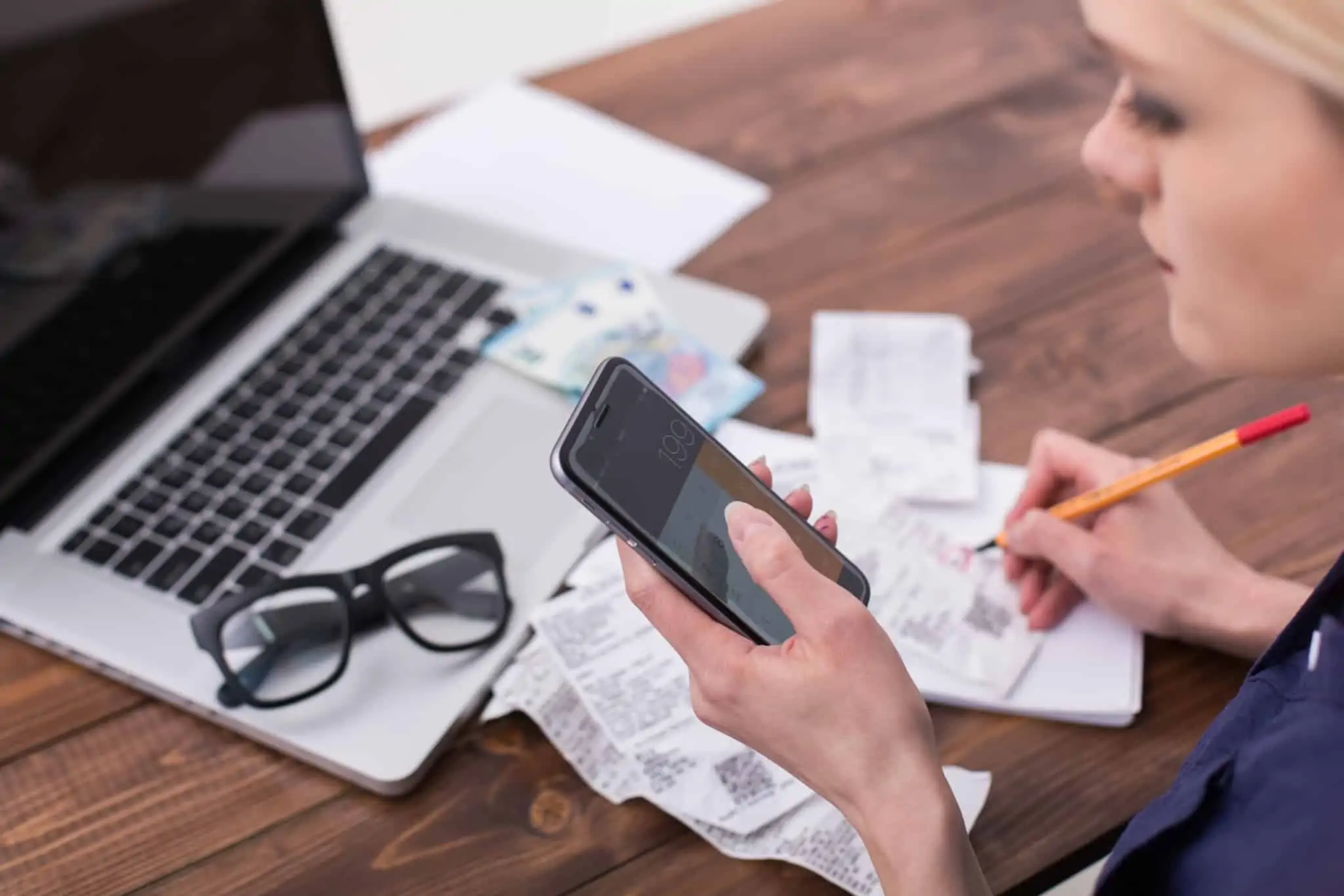 Não consegue poupar? 7 dicas para gerir o seu orçamento familiar jovem mulher lista as despesas e faz contas na calculadora do telemóvel p'ara definr o seu orçamento familiar