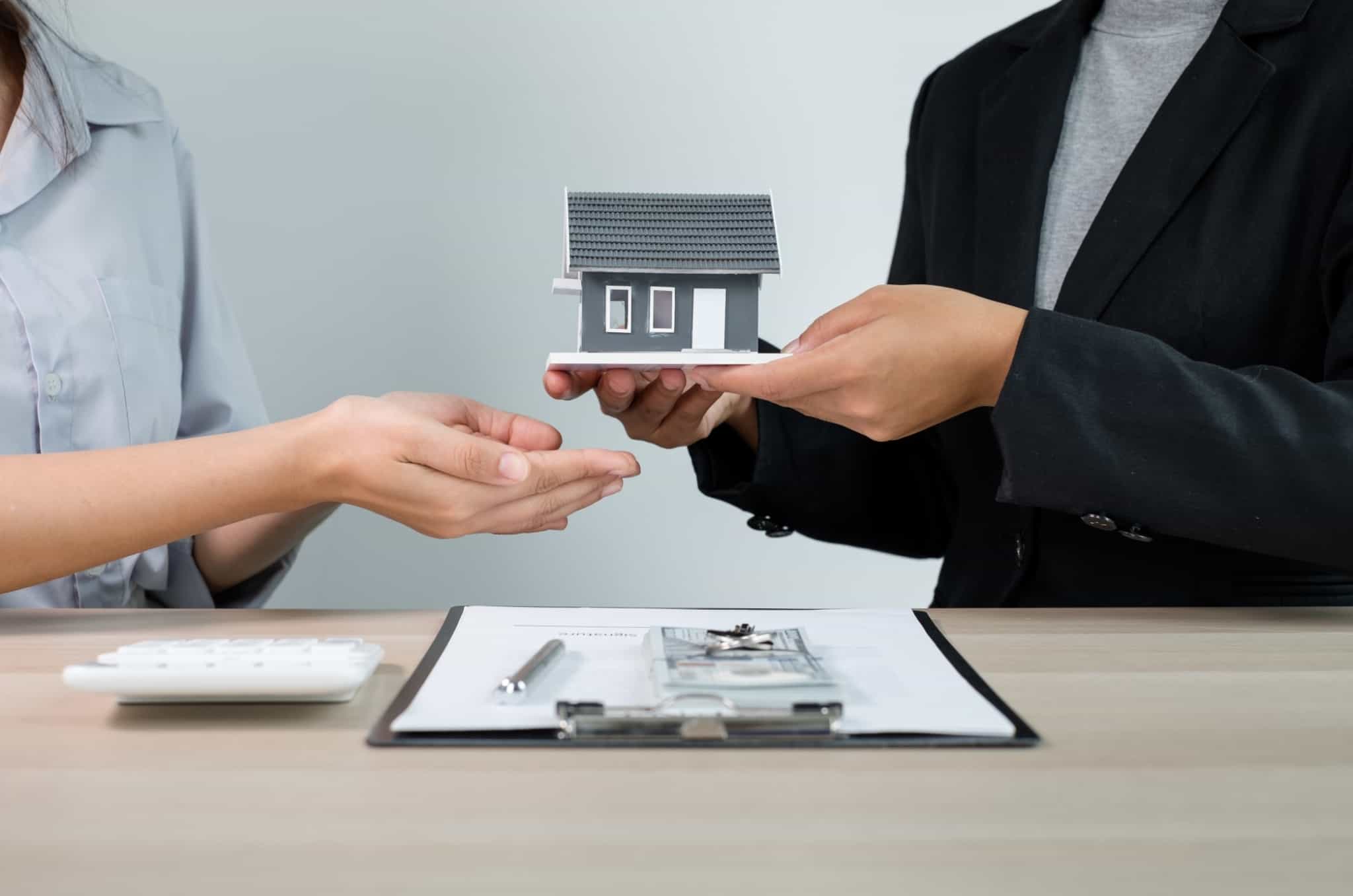 duas pessoas com uma pequena casa na mão e um contrato de crédito na mesa