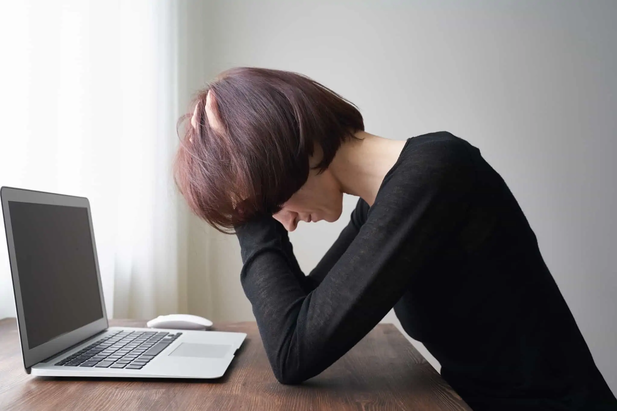 Trabalho extra: Quando e porquê deve parar? jovem mulher, exausta e de mãos na cabeça, frente ao seu computador