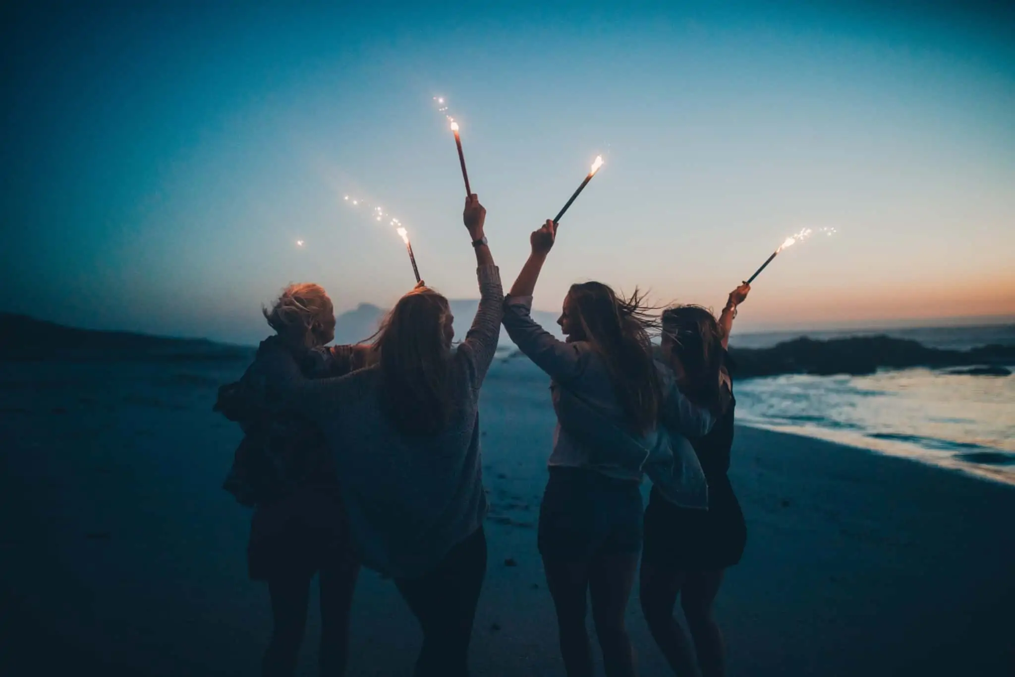 Viagem de finalistas. Que custos devo ter em conta? Colegas em viagem de finalistas de costas numa praia a segurar velas ao pôr do sol