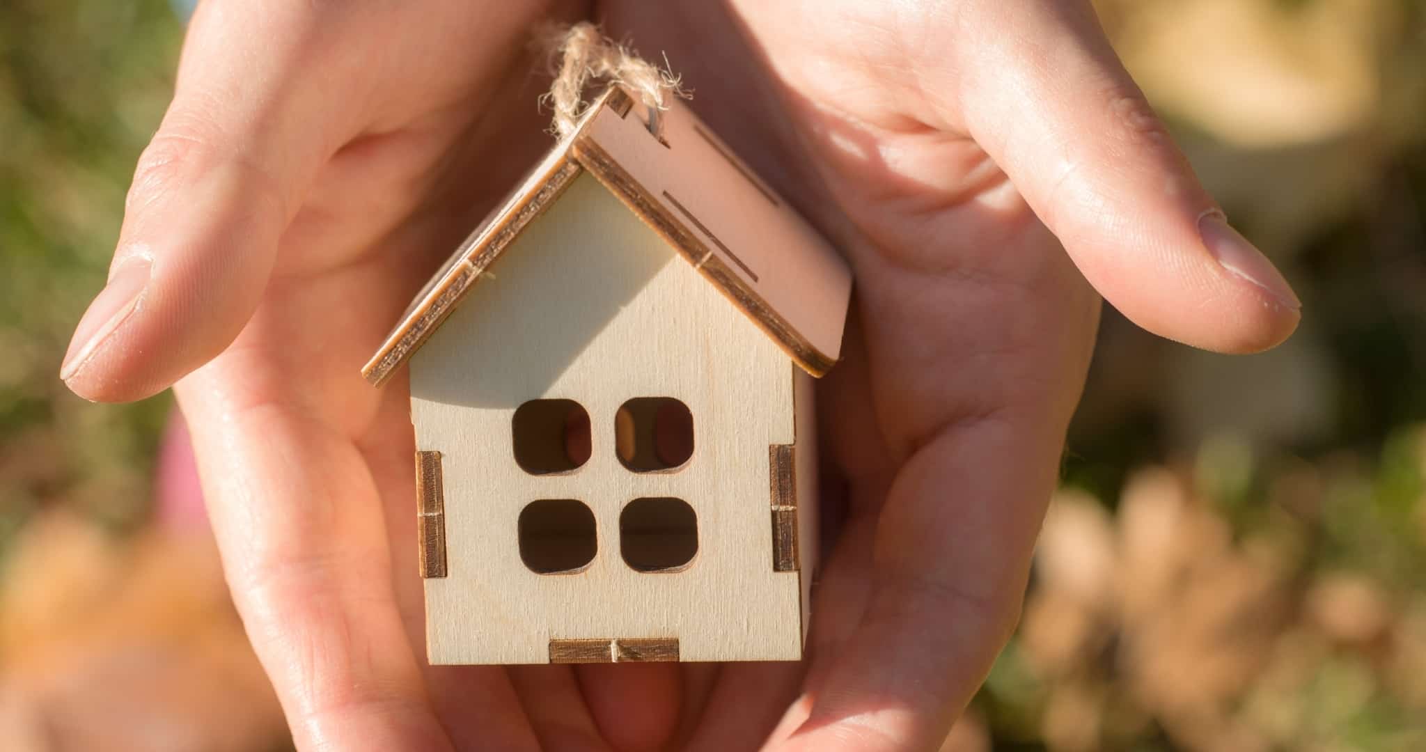 Mãos em concha a segurar casa de madeira