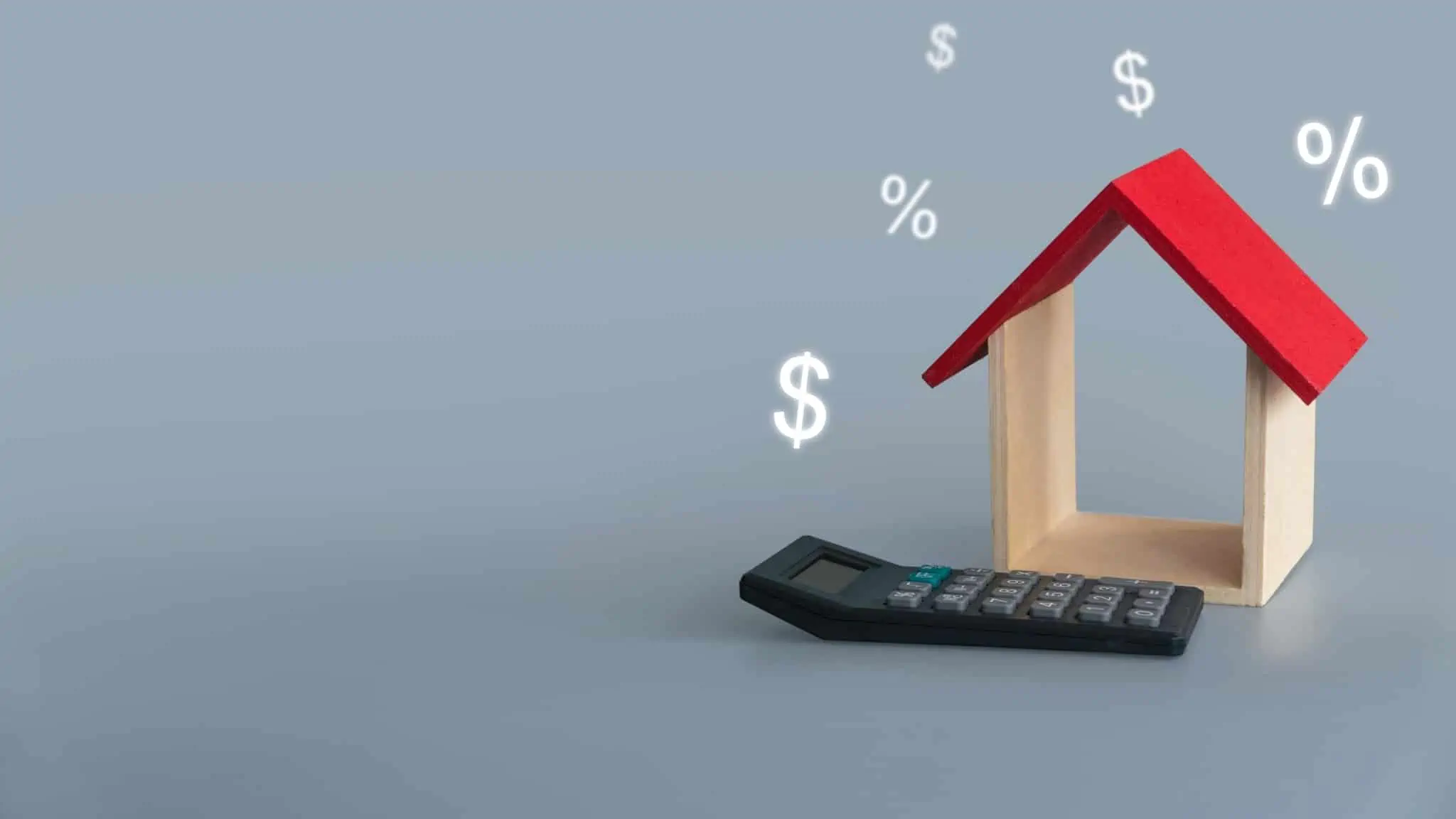 O que é o spread no crédito habitação? produção fotográfica mostra uma maqueta de uma casa, só com telhado vermelho e paredes laterais com calculadora ao pe e símbolos financeiros ao redor