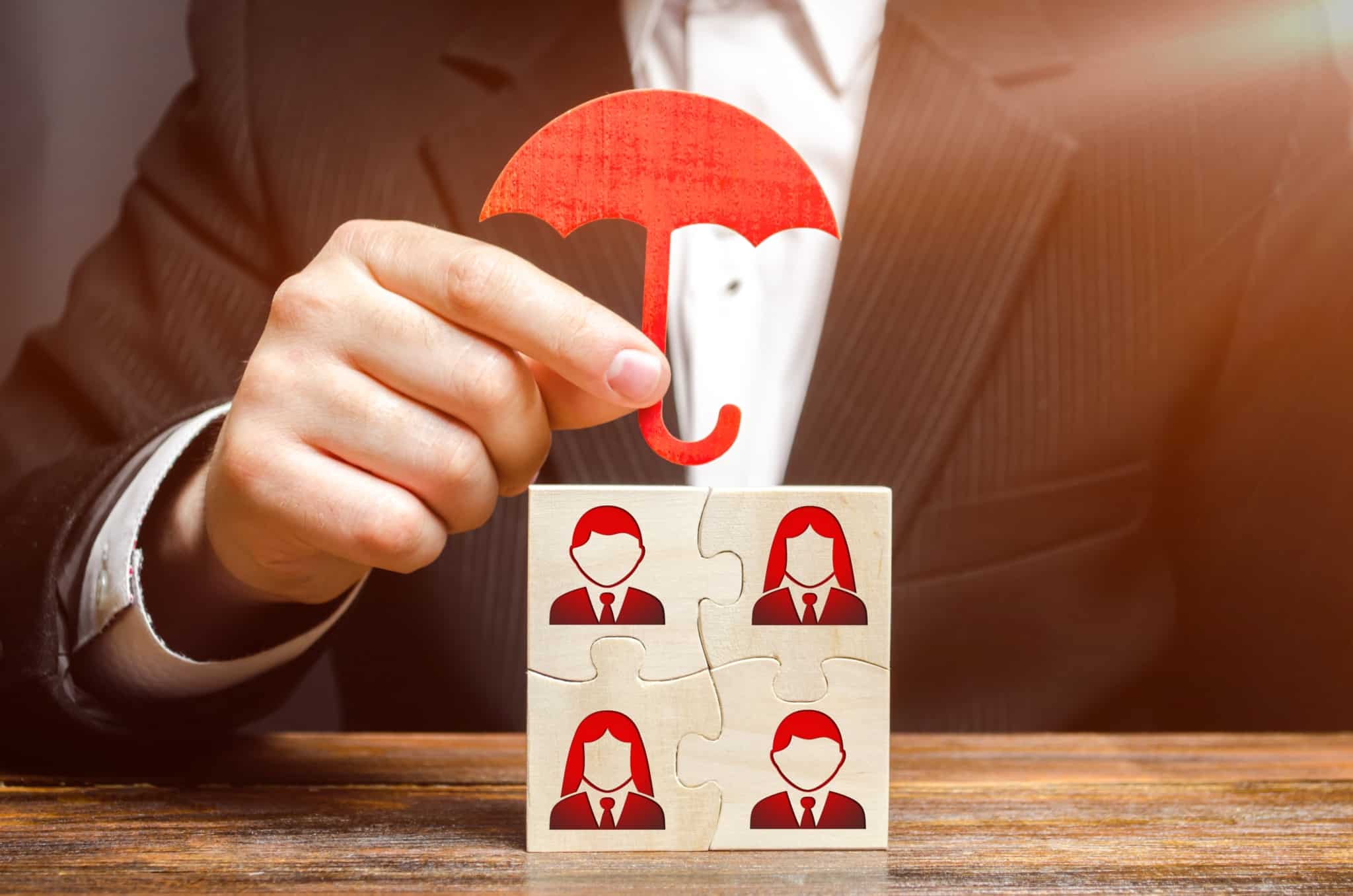 Peças de madeira encaixadas com caras estampadas e mão de senhor a cobrir as peças com um guarda-chuva