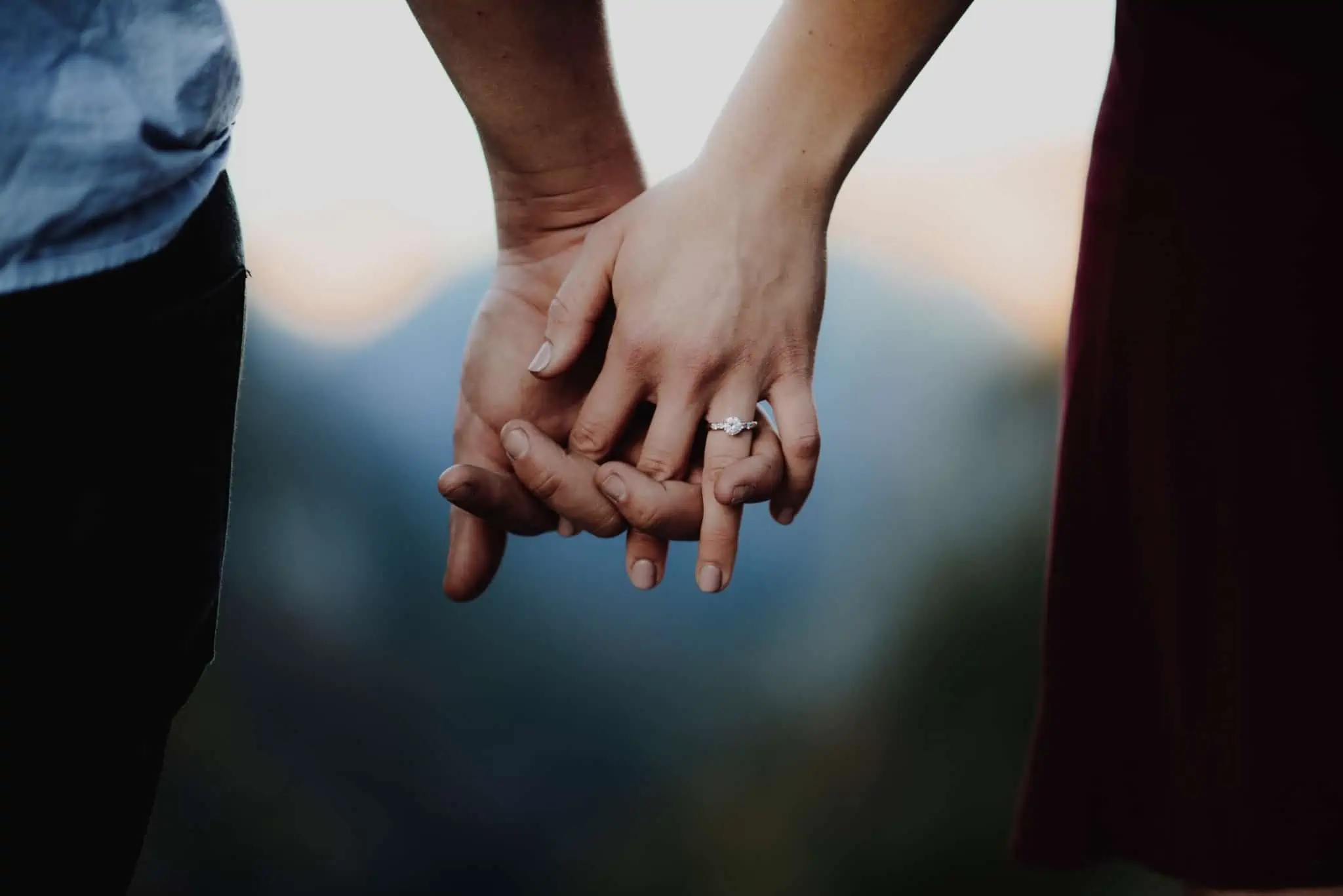 Viver em união de facto: Vantagens e desvantagens fiscais e legais produção fotográfica que mostra apenas as mãos dadas de um jovem casal, com a mulher a mostrar o anel de noivado