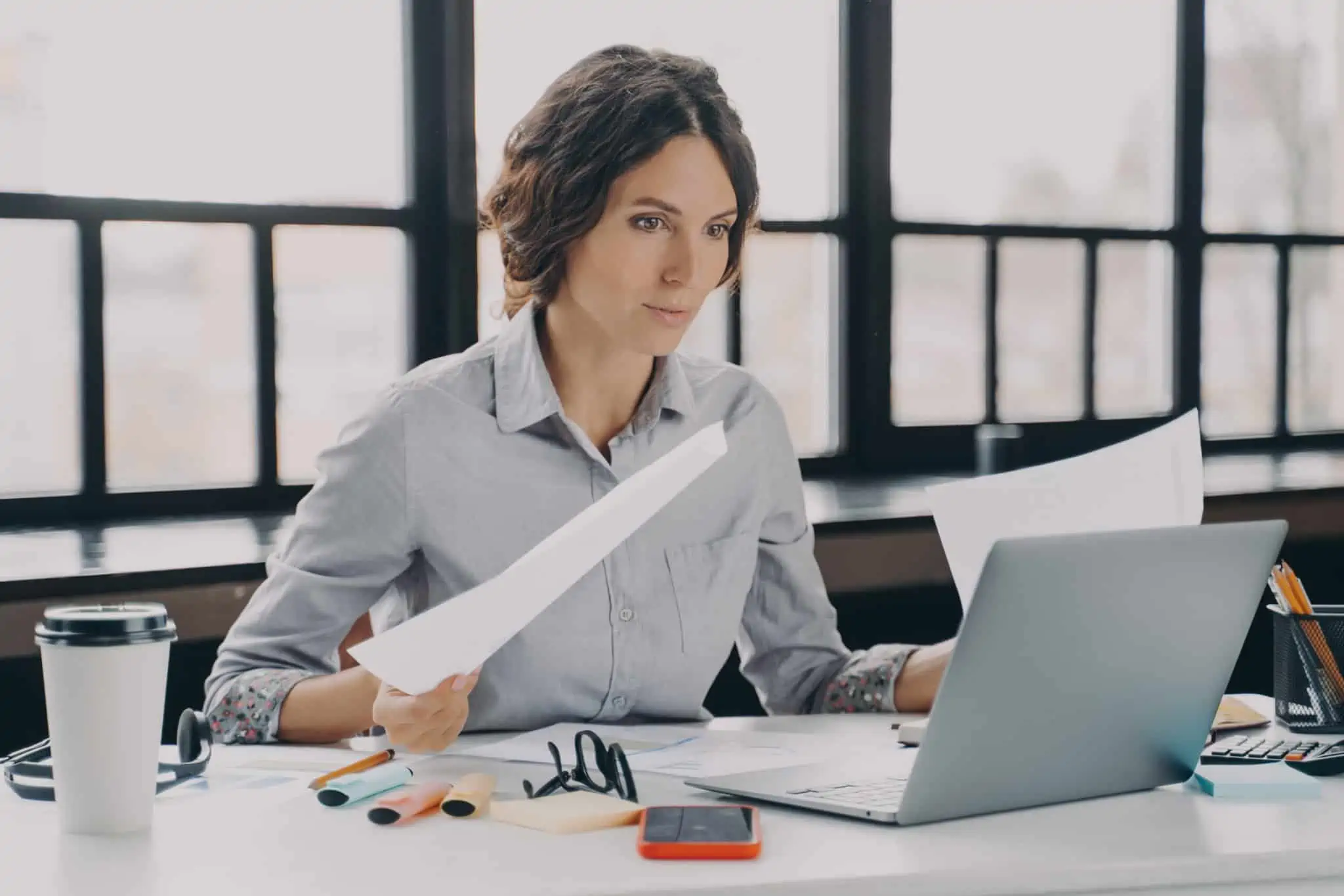 IRS: Falecimento do titular de rendimentos, como declarar? jovem mulher, ao computador e entre muita papelada, trata do IRS para declarar falecimento do titular de rendimentos
