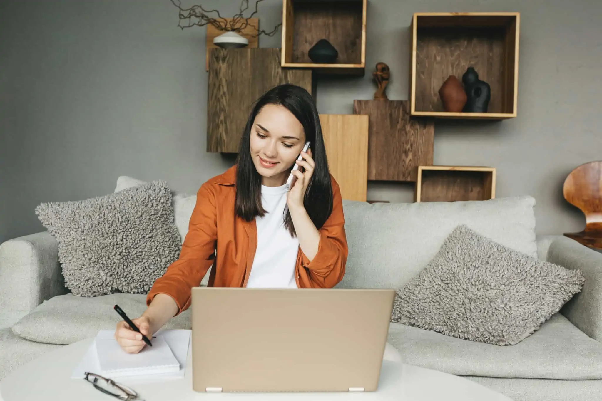 Seguro de acidentes de trabalho para trabalhadores independentes: Como funciona? uma trabalhadora independente sentada com o computador à frente enquanto fala ao telefone e tira apontamentos