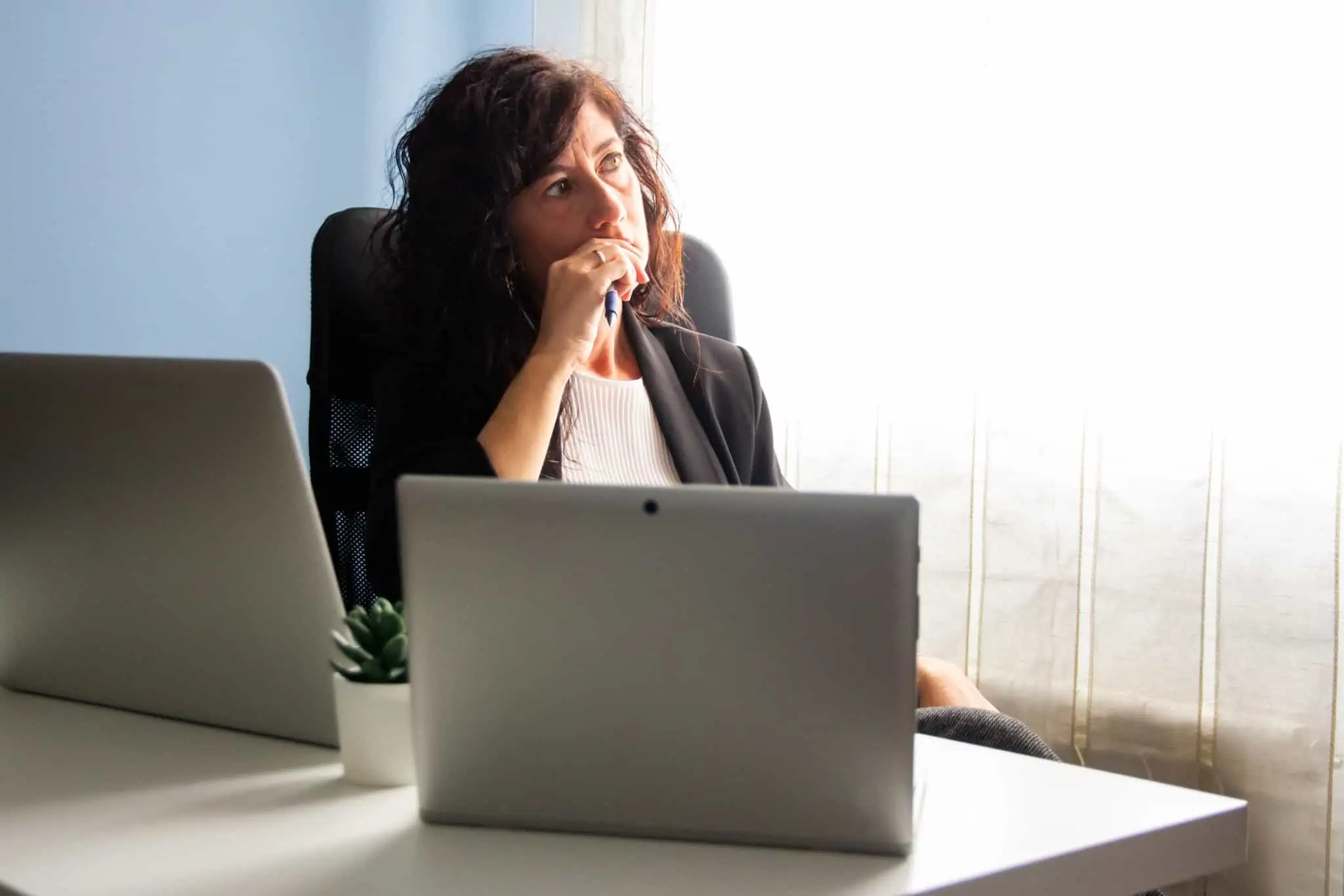 Cancelar a conta bancária após um falecimento: Quais os passos a dar mulher sentada frente aos computadores de olhar triste e pensativa, como que a questionar-se ou a refletir