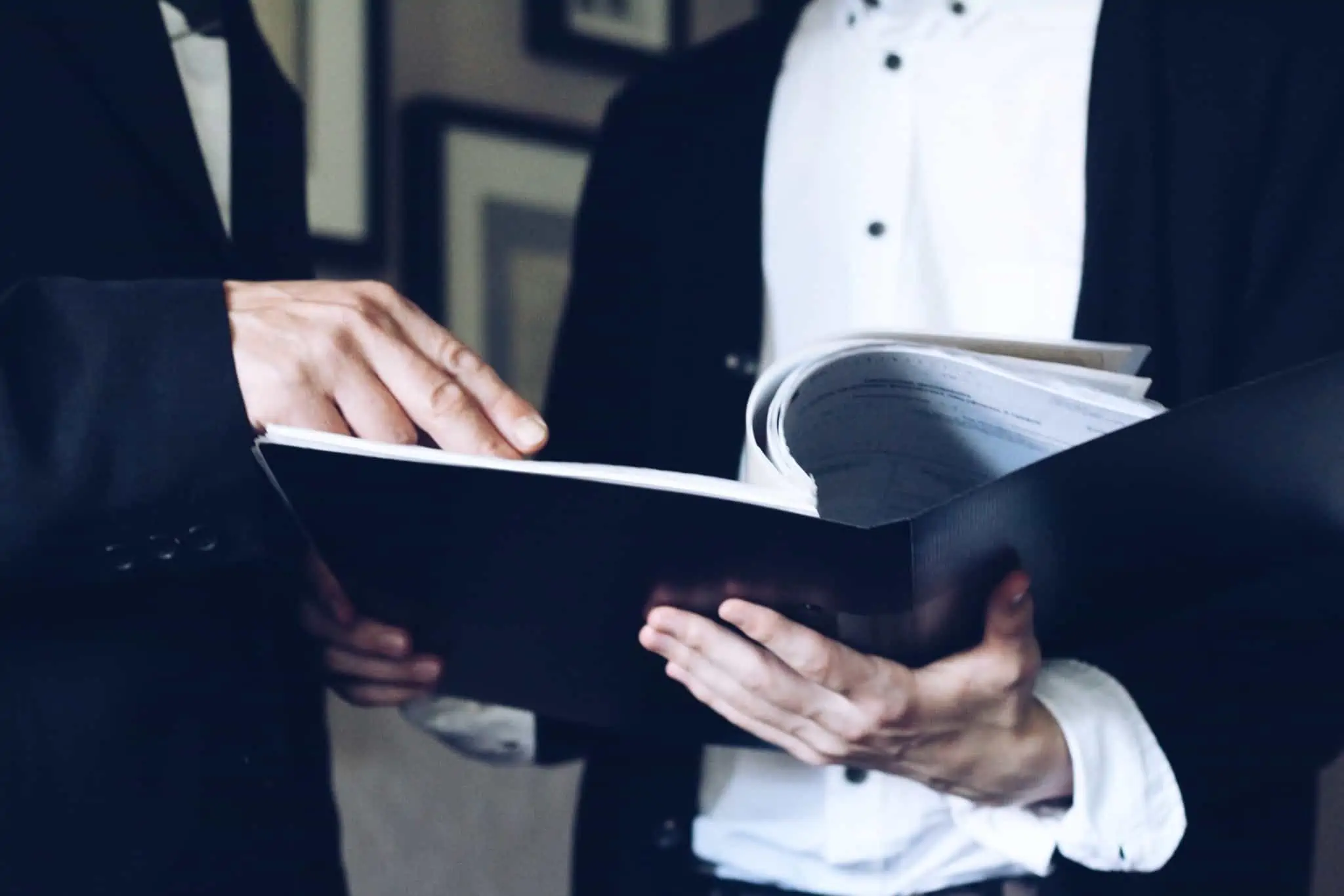 Crédito pessoal: O que é preciso para ter o empréstimo aprovado? pasta aberta com documentos nas mãos de um homem, sendo que um outro aponta para a folha que estão a analisar
