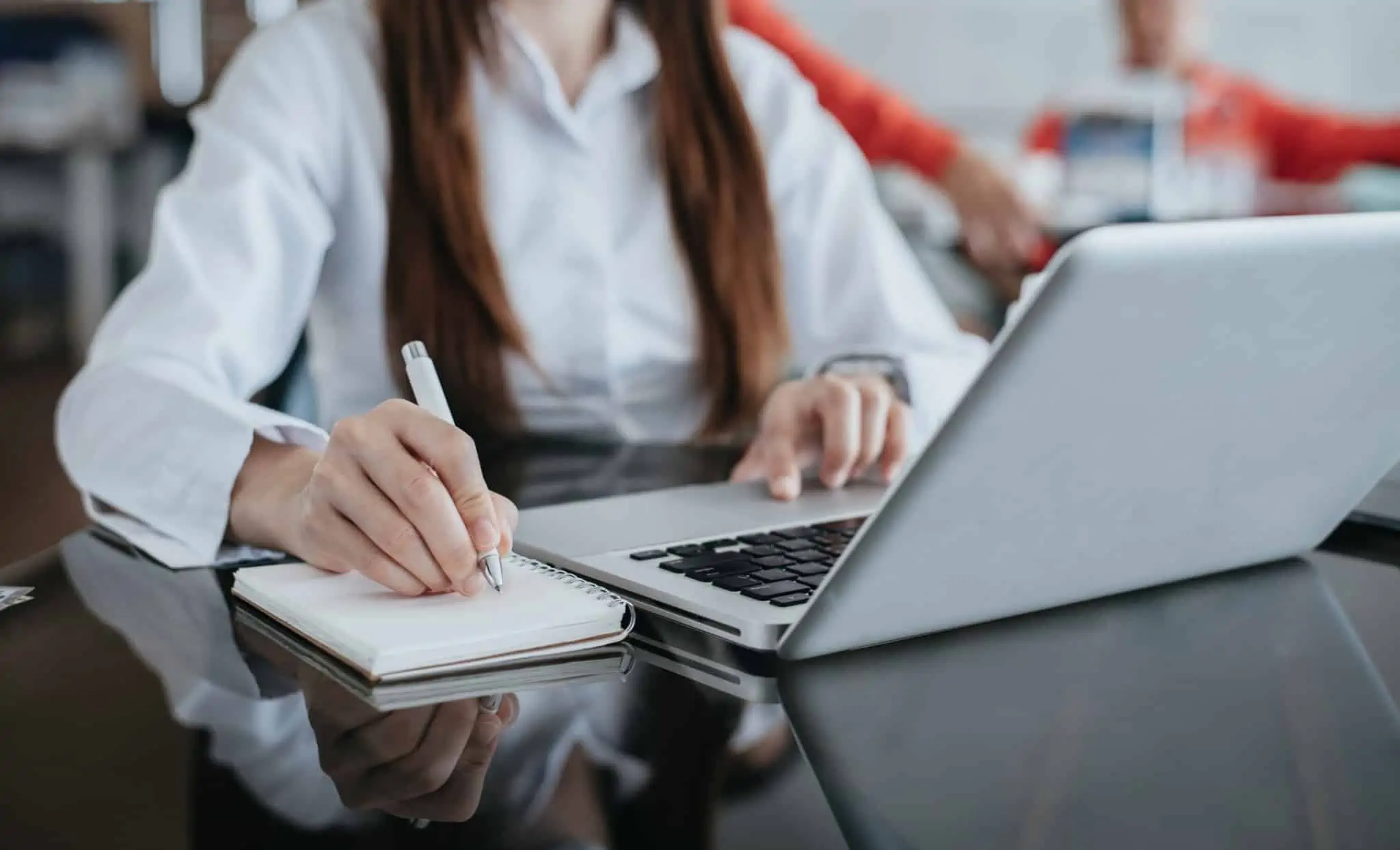 Débito direto para impostos: Como aderir e quais posso pagar? jovem mulher usa o computador portátil para ar ordem para débito direto no pagamento de impostos, enquanto tira notas para um caderno