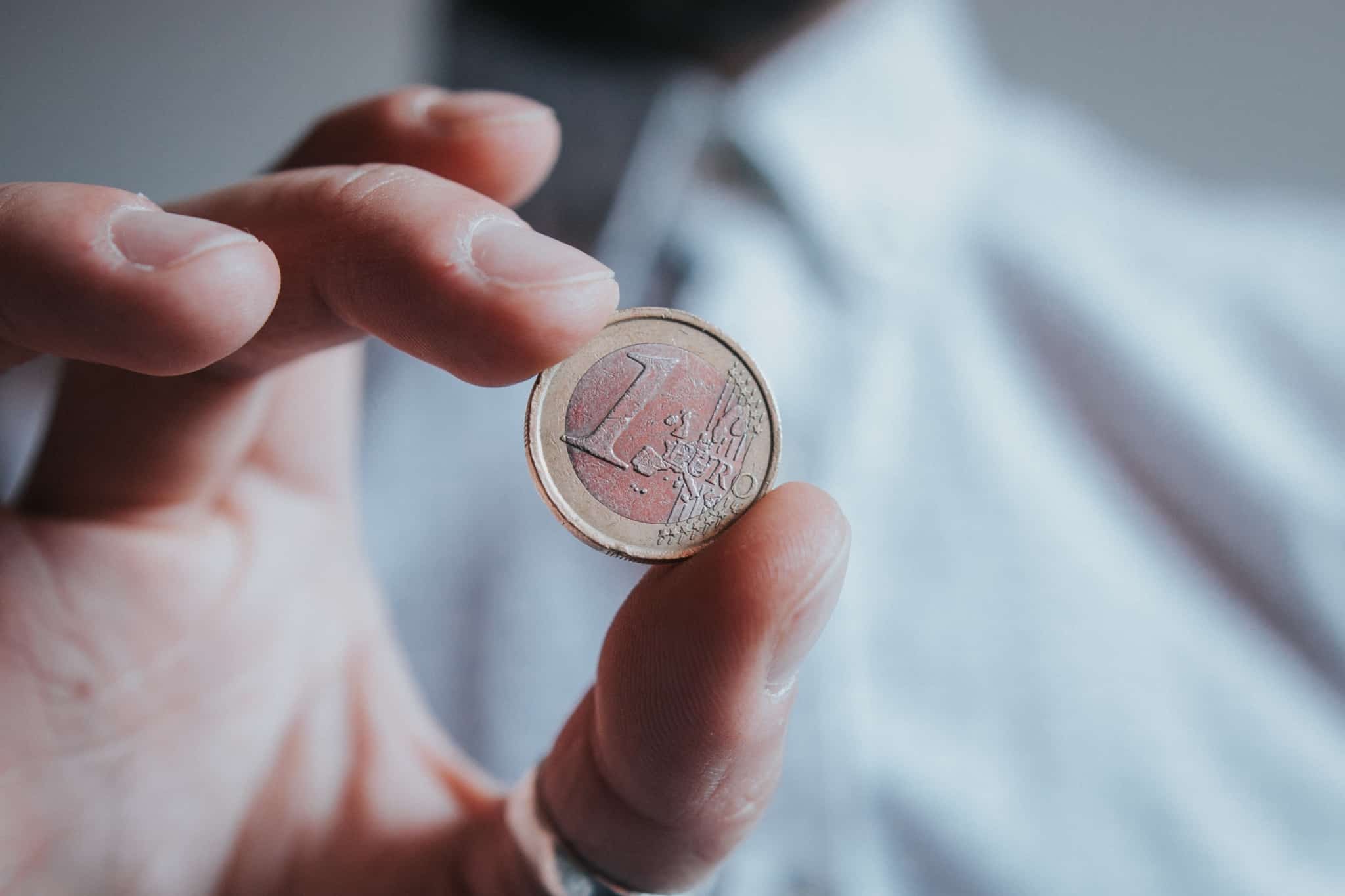 com fundo desfocado um homem segura entre os dedos uma moeda de 1 euro