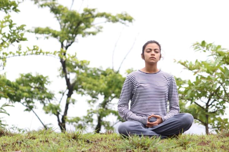 Jovem está a meditar no meio da natureza, num exercício para ter uma vida mais saudável