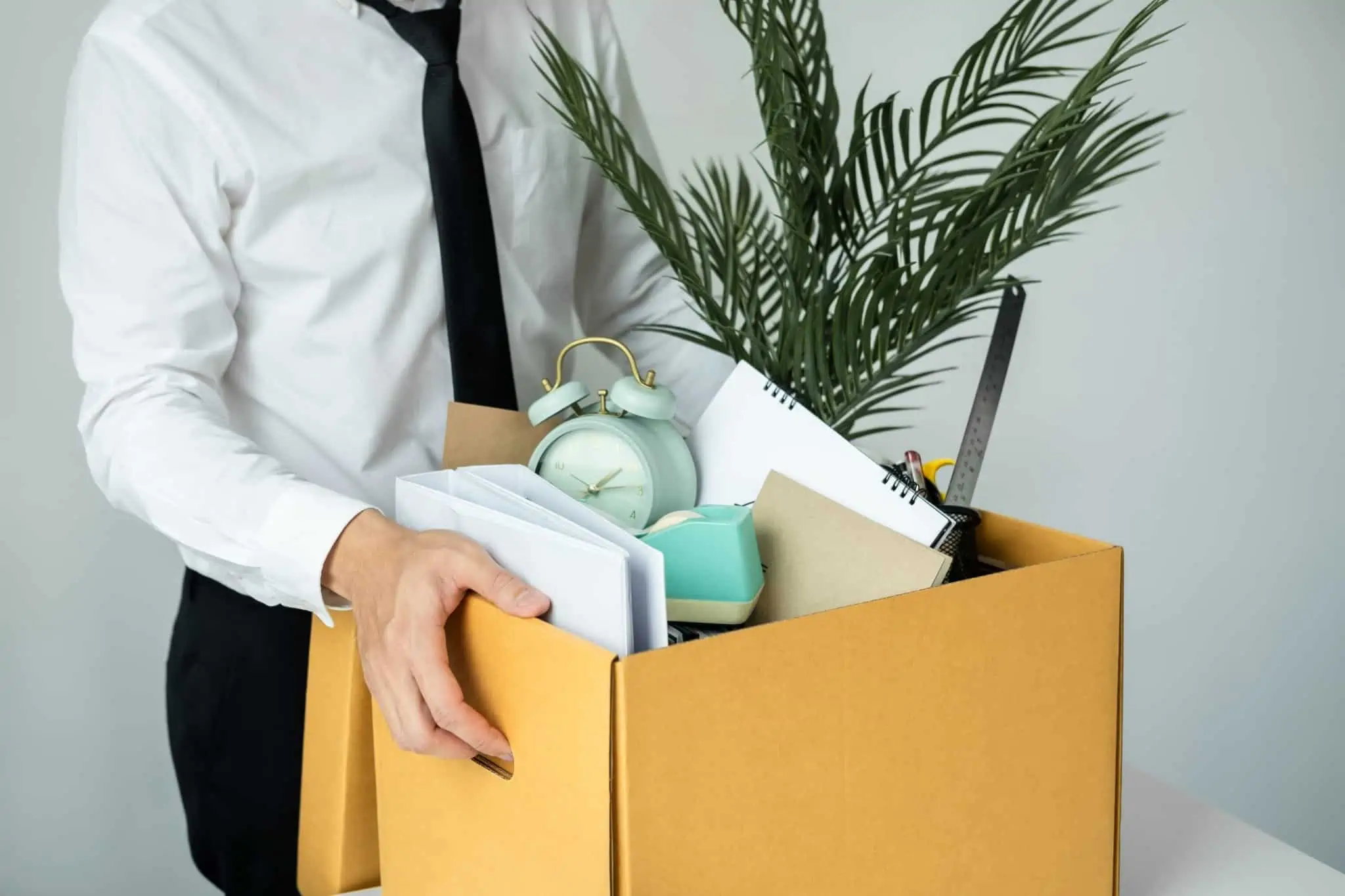 É possível recusar uma proposta de emprego do IEFP? jovem homem carrega uma caixa de cartão com todos o bens pessoais, como relogio de mesa de escritório e pastas com documentos, na sequência de ter perdido o emprego