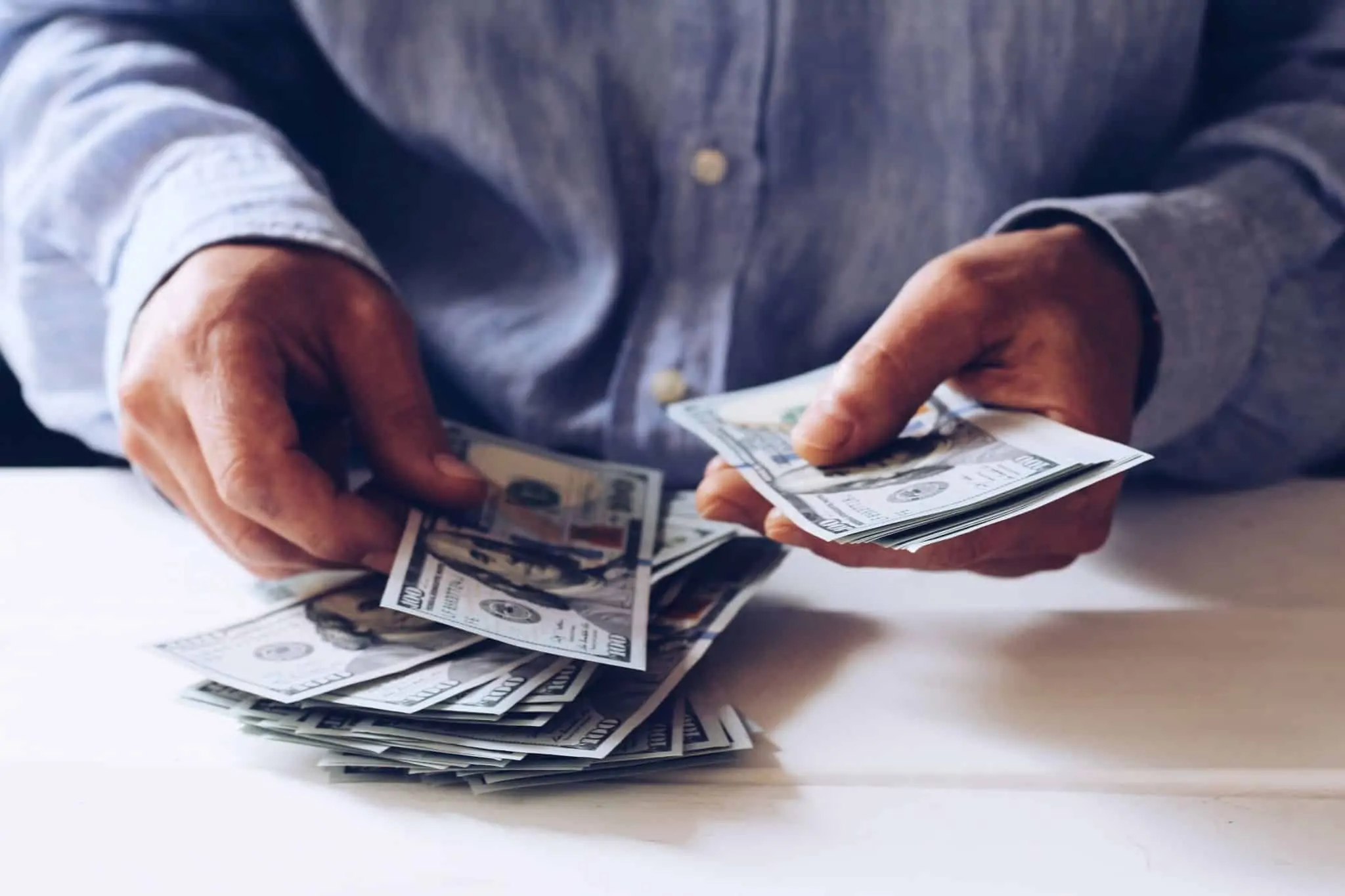 Tem rendimentos no estrangeiro? Saiba o que fazer no IRS Imagem de alguém a contar notas de dólar à mesa - numa alusão aos rendimentos obtidos no estrangeiro para efeitos de irs