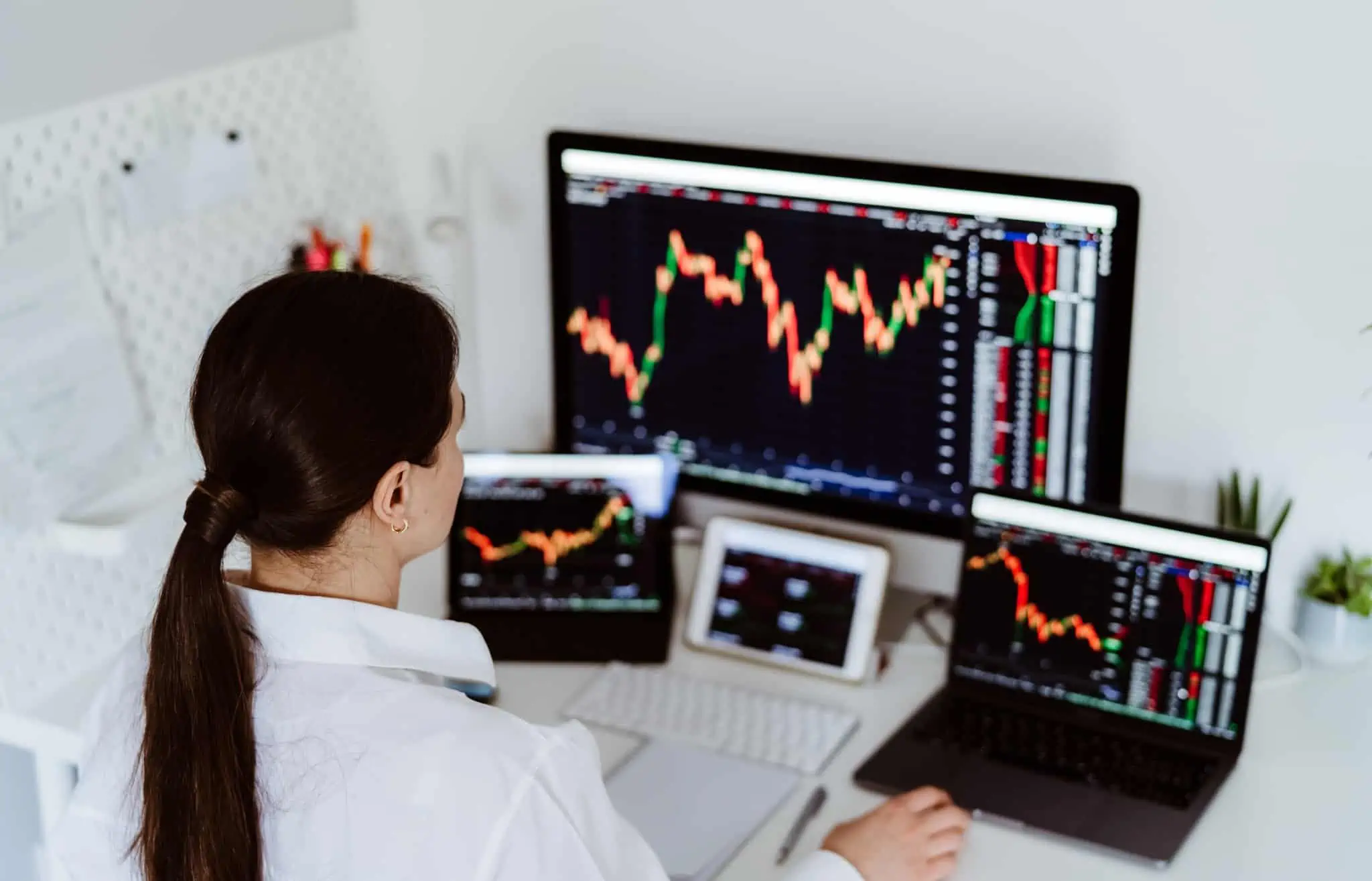Registei mais-valias em investimentos, devo preencher o anexo E do IRS? mulher em frente a vários ecrãs com gráficos de investimentos e a analisar as mais-valias em investimentos para preencher o anexo E do IRS